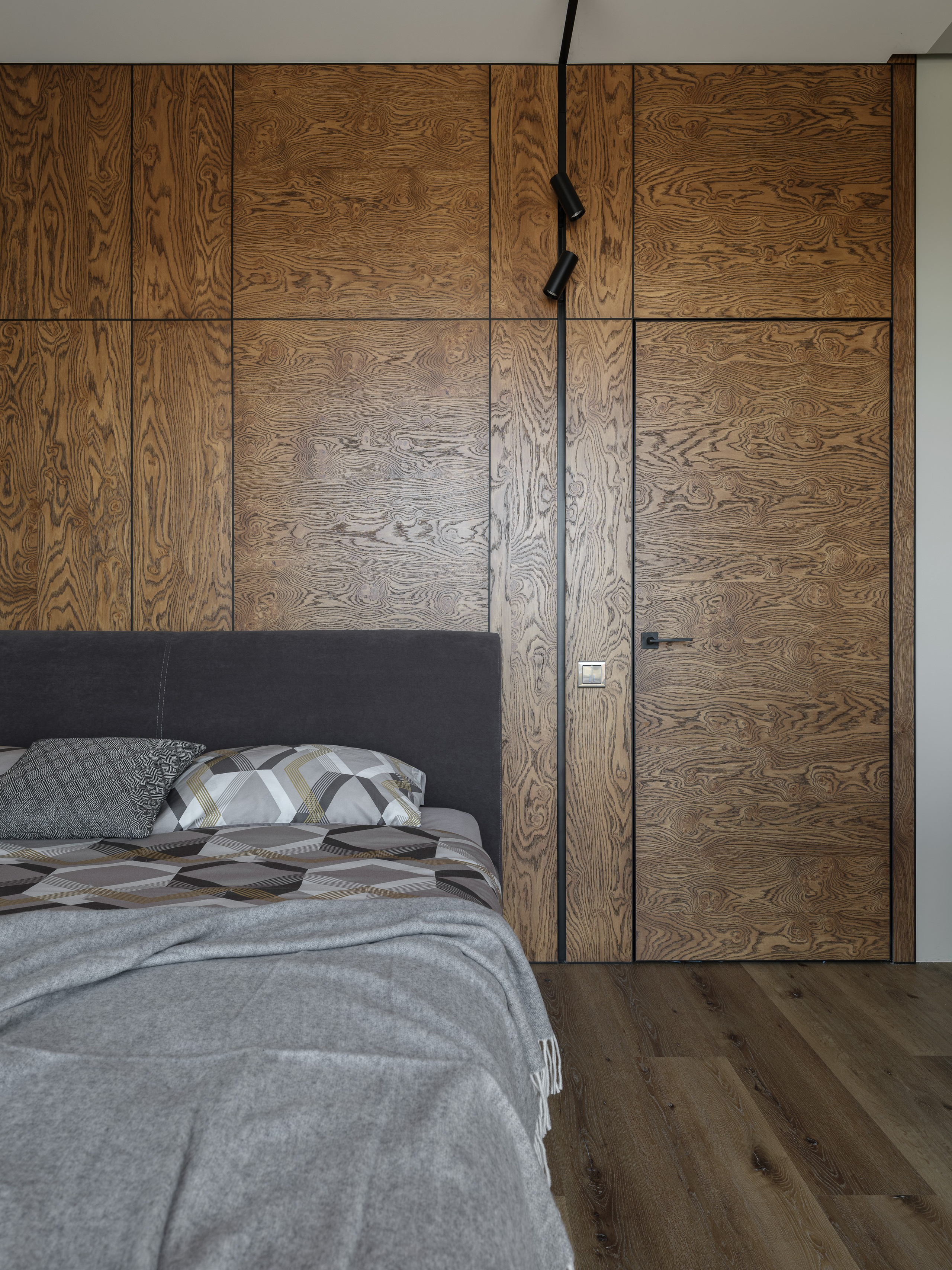 Фрагмент спальни с деревянными панелями на стене, серым изголовьем и спокойной геометрией текстиля. Интерьер выполнен дизайнером Алиной Дёровой при стилизации Натальи Якушевой, фото Сергея Денисенко.