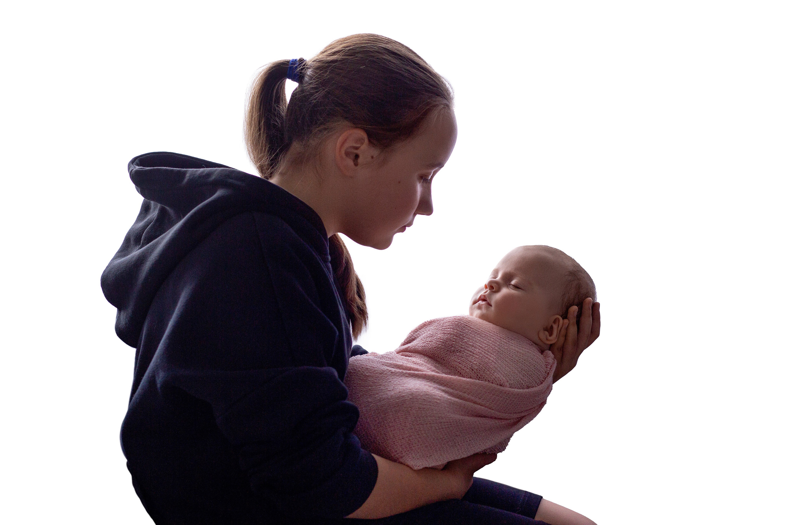 портрет - старшая сестричка сидит на белом фоне в темном худи и держит на руках спящую новорожденную младшую сестру