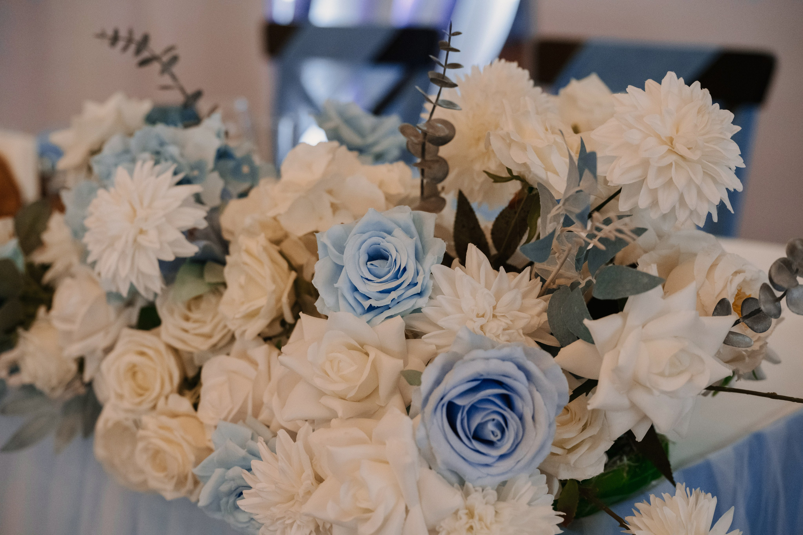 Букет белых и голубых цветов стоит на столе, украшая свадебный стол жениха и невесты