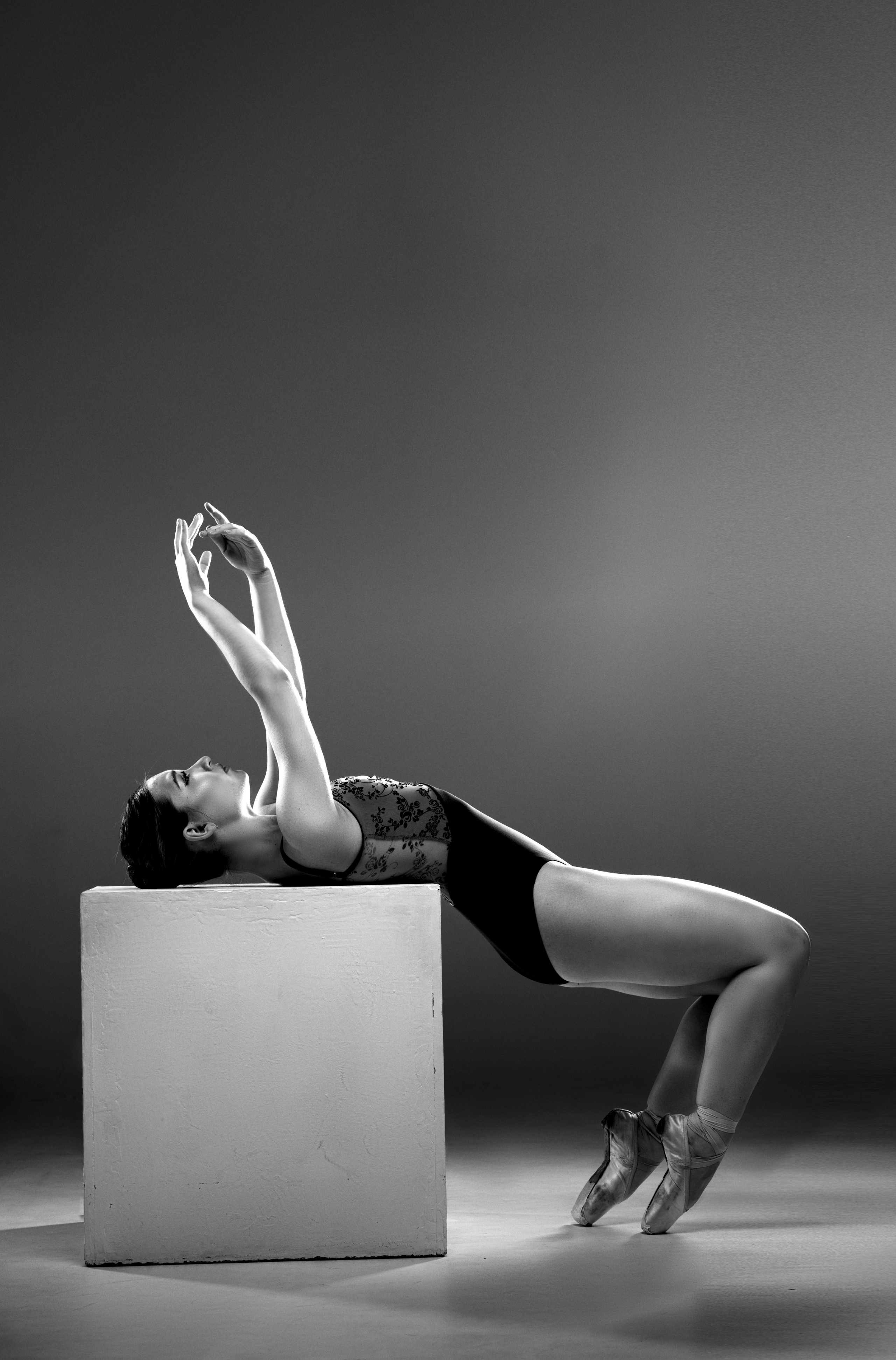 Портфолио балерины: художественная балетная съемка в стиле спорт-арт. Черно-белая фотография балерины в черном купальнике, опирающейся на белый куб.