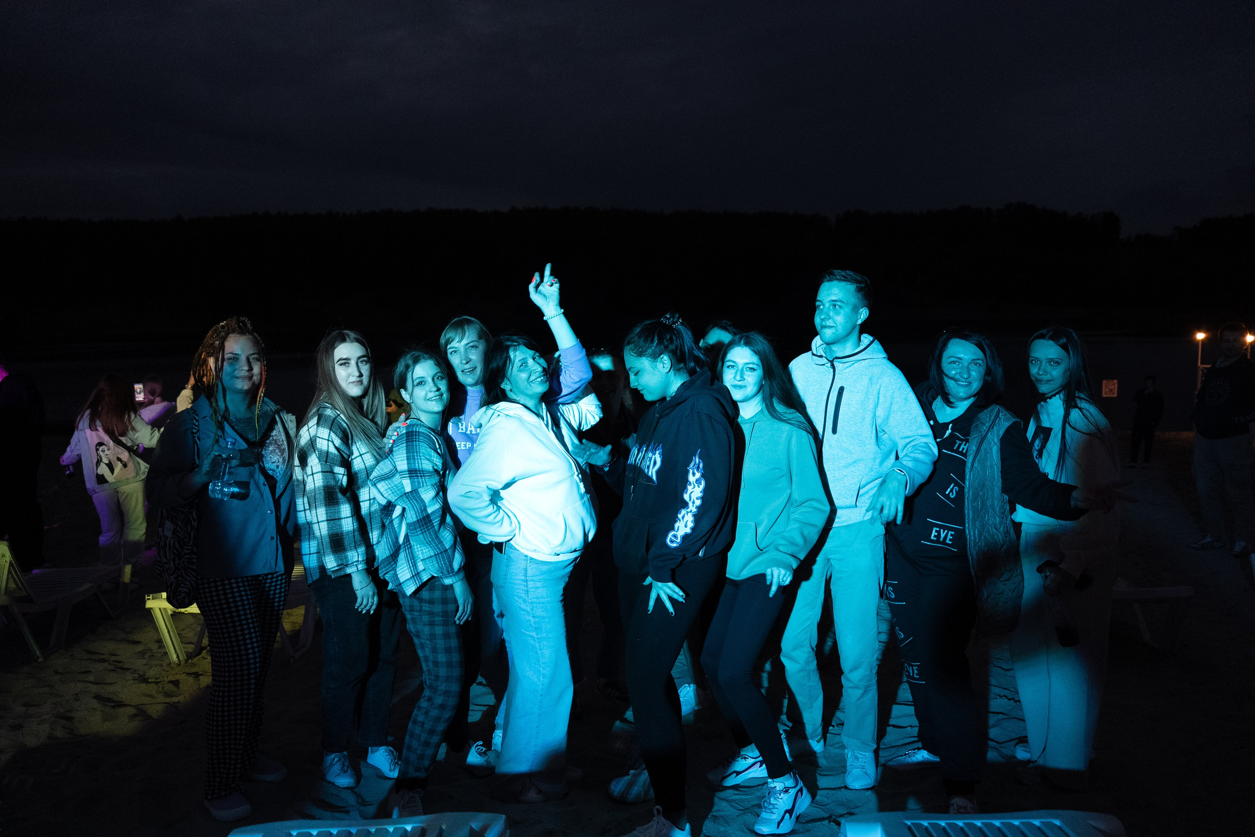 Молодежная вечеринка на пляже ночью, группа друзей танцует на песке, светлые лежаки