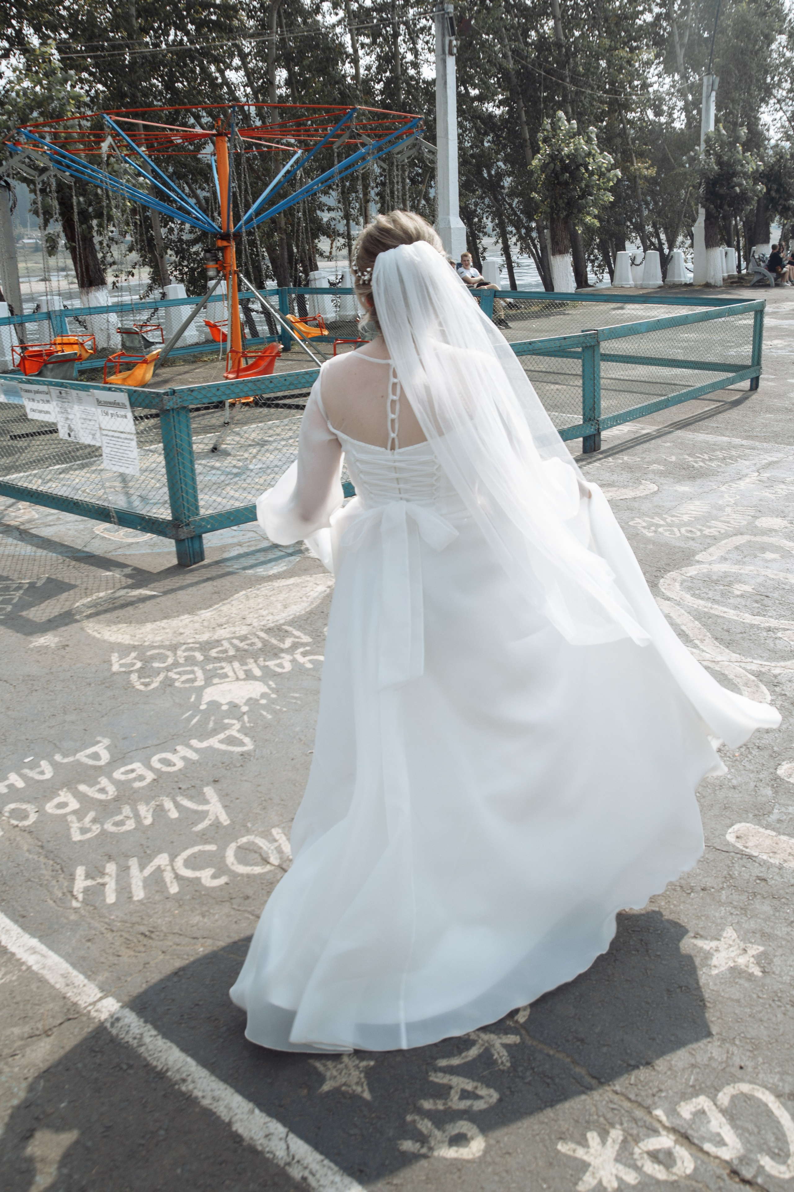  Невеста в белом платье идёт по аллее с рисунками и подписями, держась за платье.