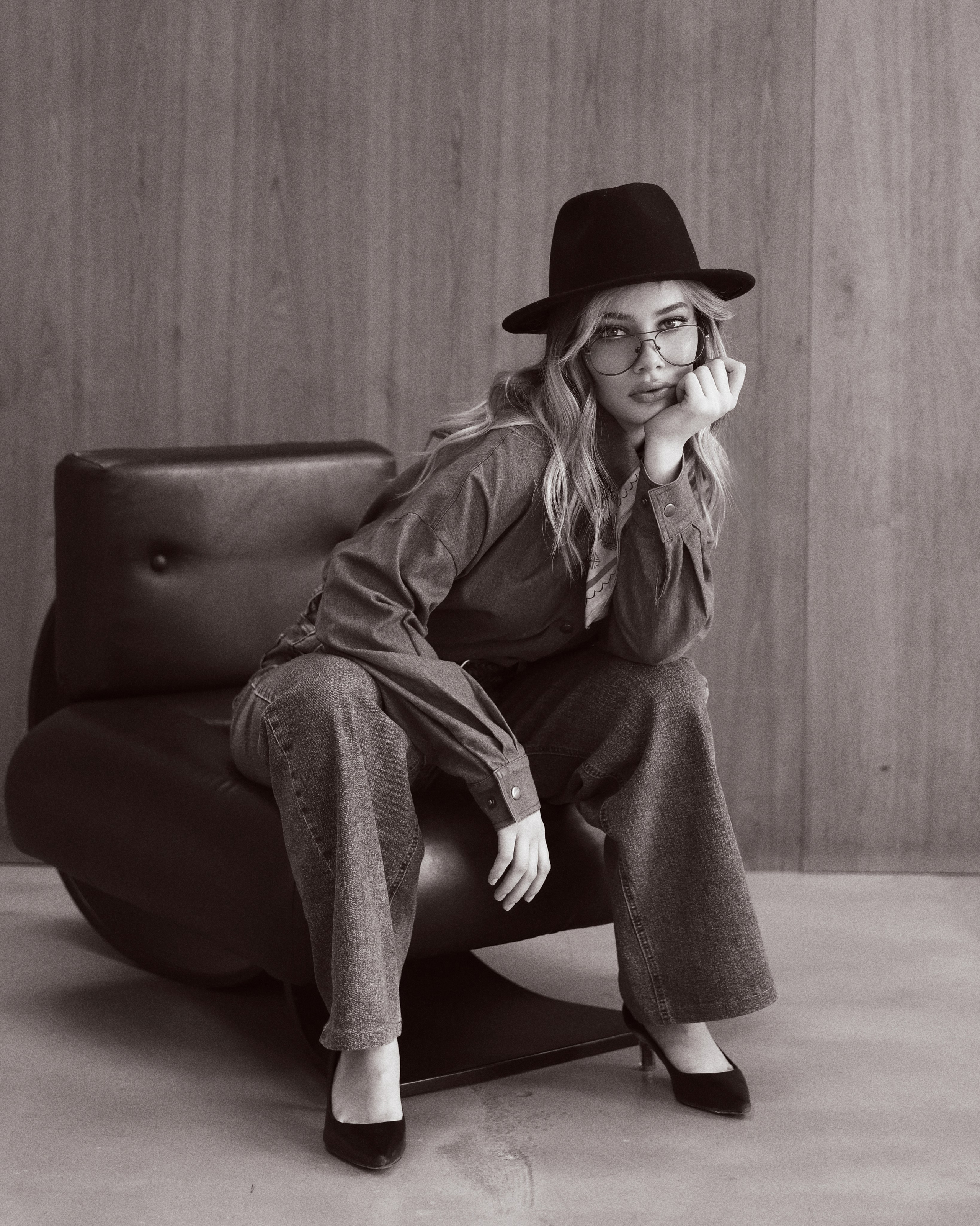 Фотосессия Челябинск в студии для девушки - стильная студийная фотосъемка в модном образе, девушка в джинсовой рубашке и джинсах с ремнем, в черной шляпе и очках позирует на фоне темных штор, fashion фотосессия в студии Челябинск, трендовый образ, городская эстетика, уверенная поза, профессиональная фотосессия для девушек, идеи для фотосессии в студии, стиль casual и fashion, съемка для личного бренда и инстаграм, современная портретная съемка, выразительный взгляд, мягкий студийный свет, красивая фотосессия Челябинск, услуги фотографа Челябинск, студийная фотосъемка для контента, вдохновение для фотосессии, позирование для девушек, стильная фотосессия в темной студии