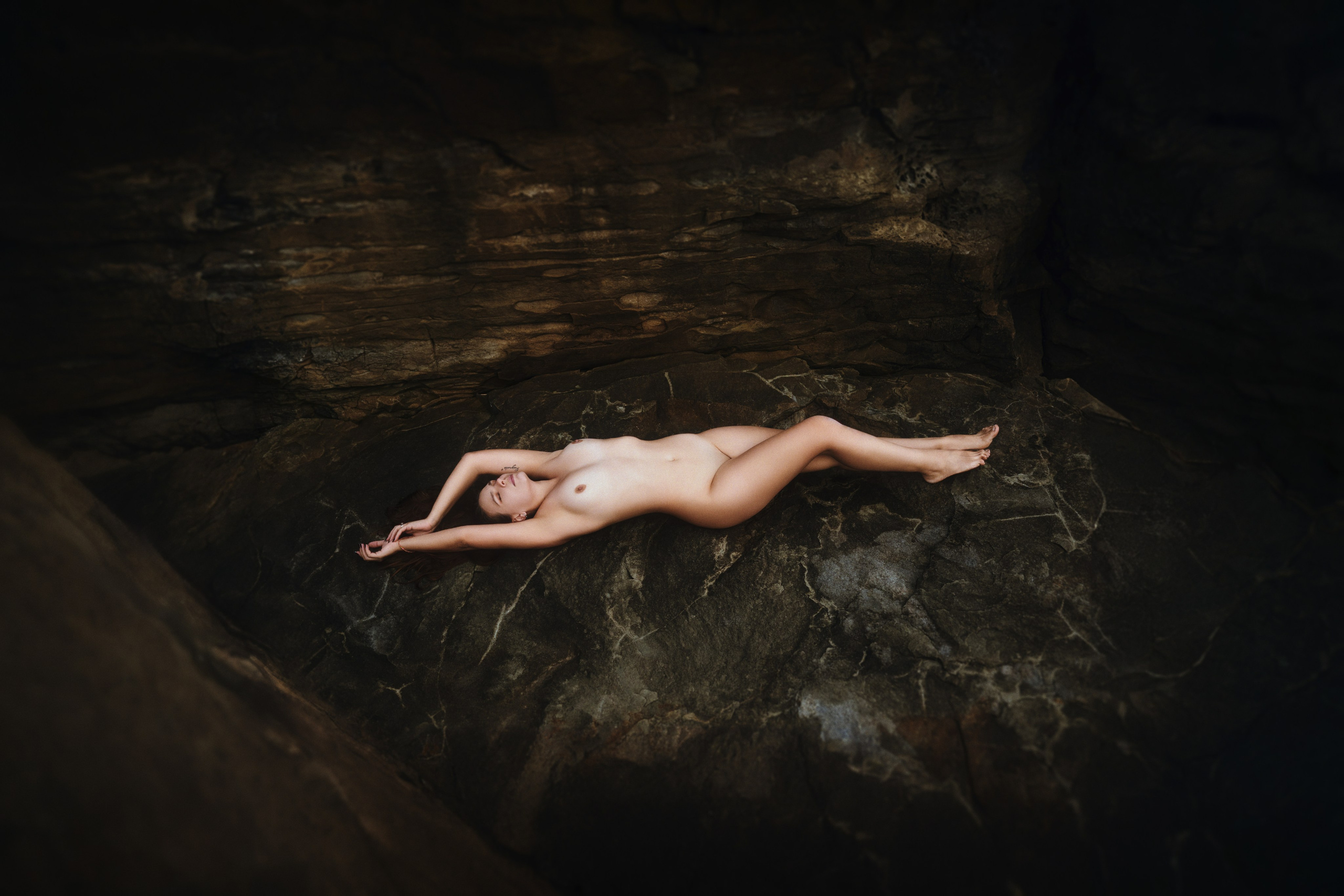 Атлетичная обнажённая женщина лежит на скале - пример позы для фотосессии ню