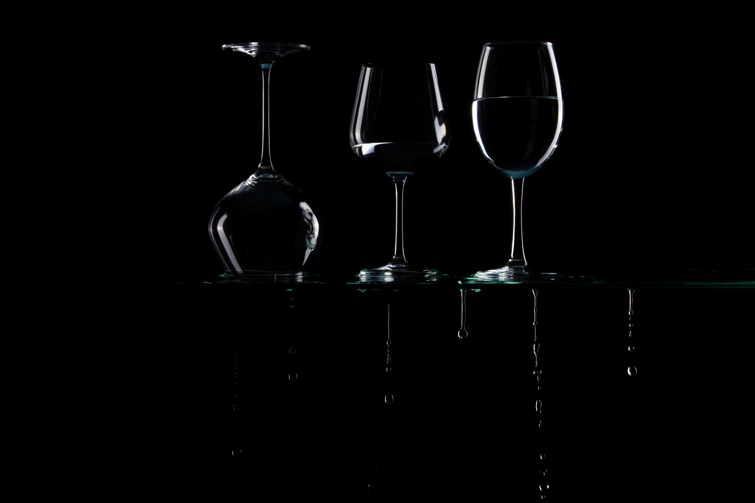 Контуры стеклянных бокалов тонко очерчены светом на чёрном фоне с каплями. 