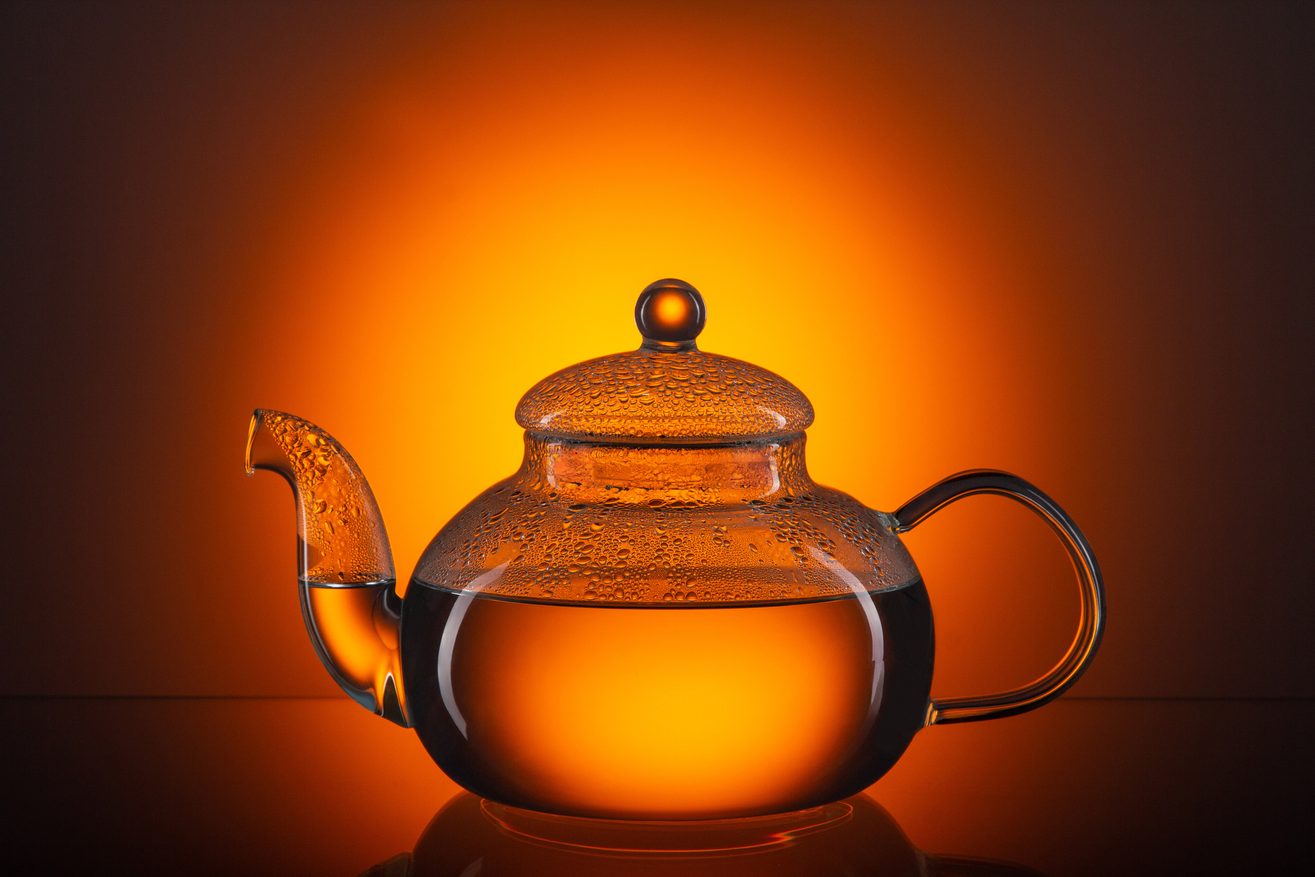 Заварной стеклянный чайник с чаем в красивом ракурсе на фоне оранжевого заката.