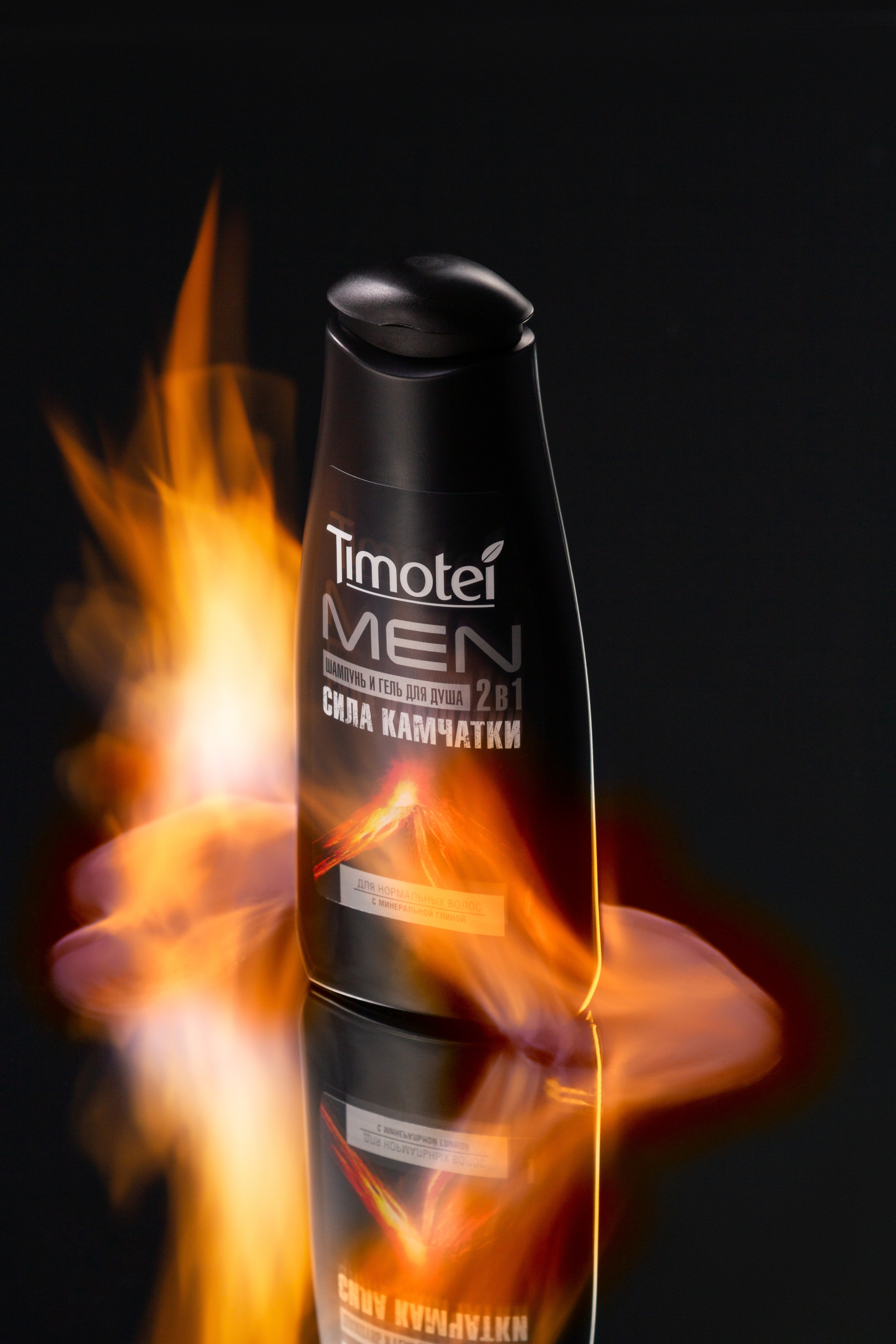 Чёрная бутылочка шампуни в огне на зеркальной поверхности на чёрном фоне.