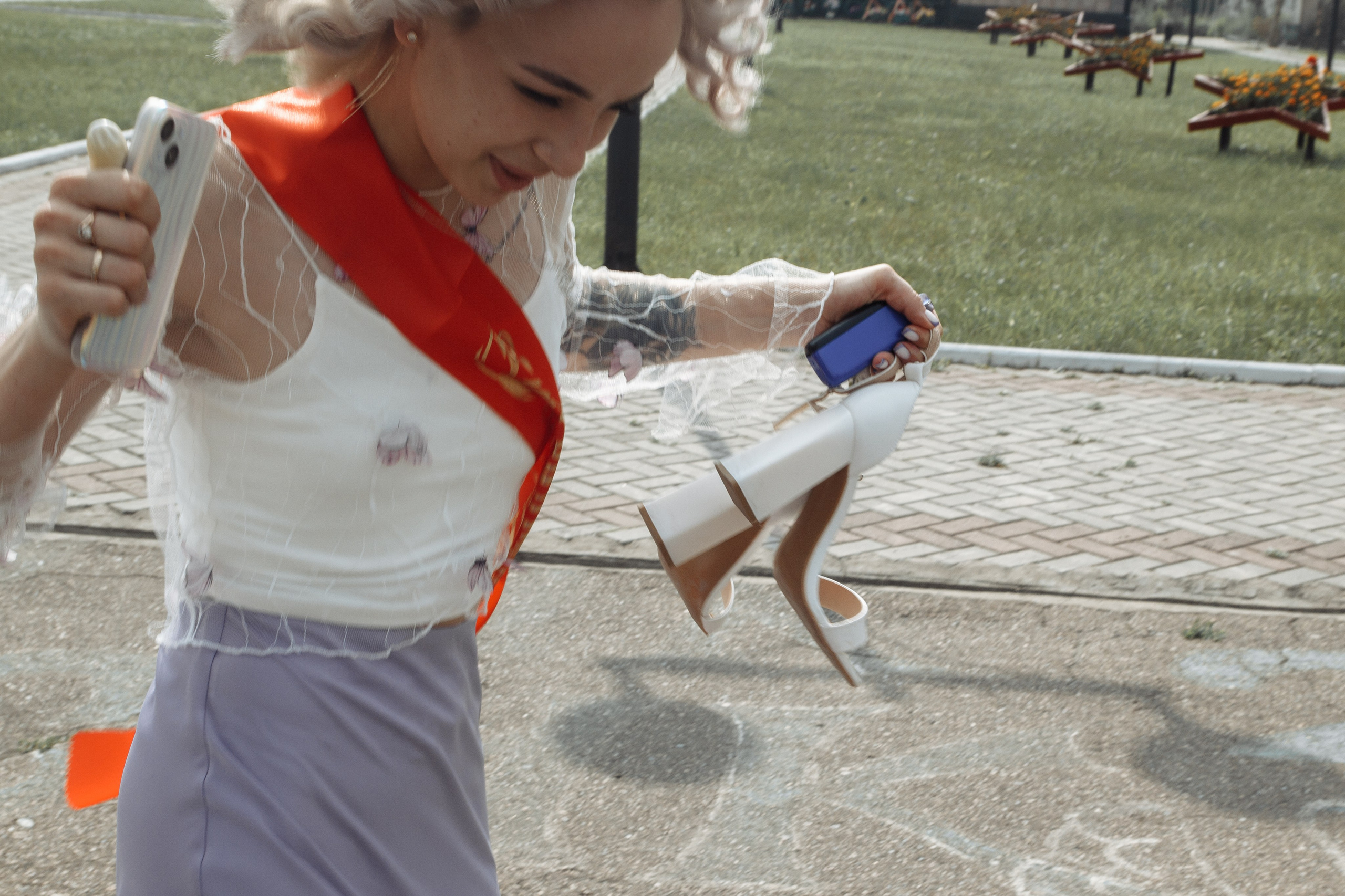 Девушка в ленте свидетельницы танцует на открытом воздухе — весёлый момент на фоне свадебного дня.