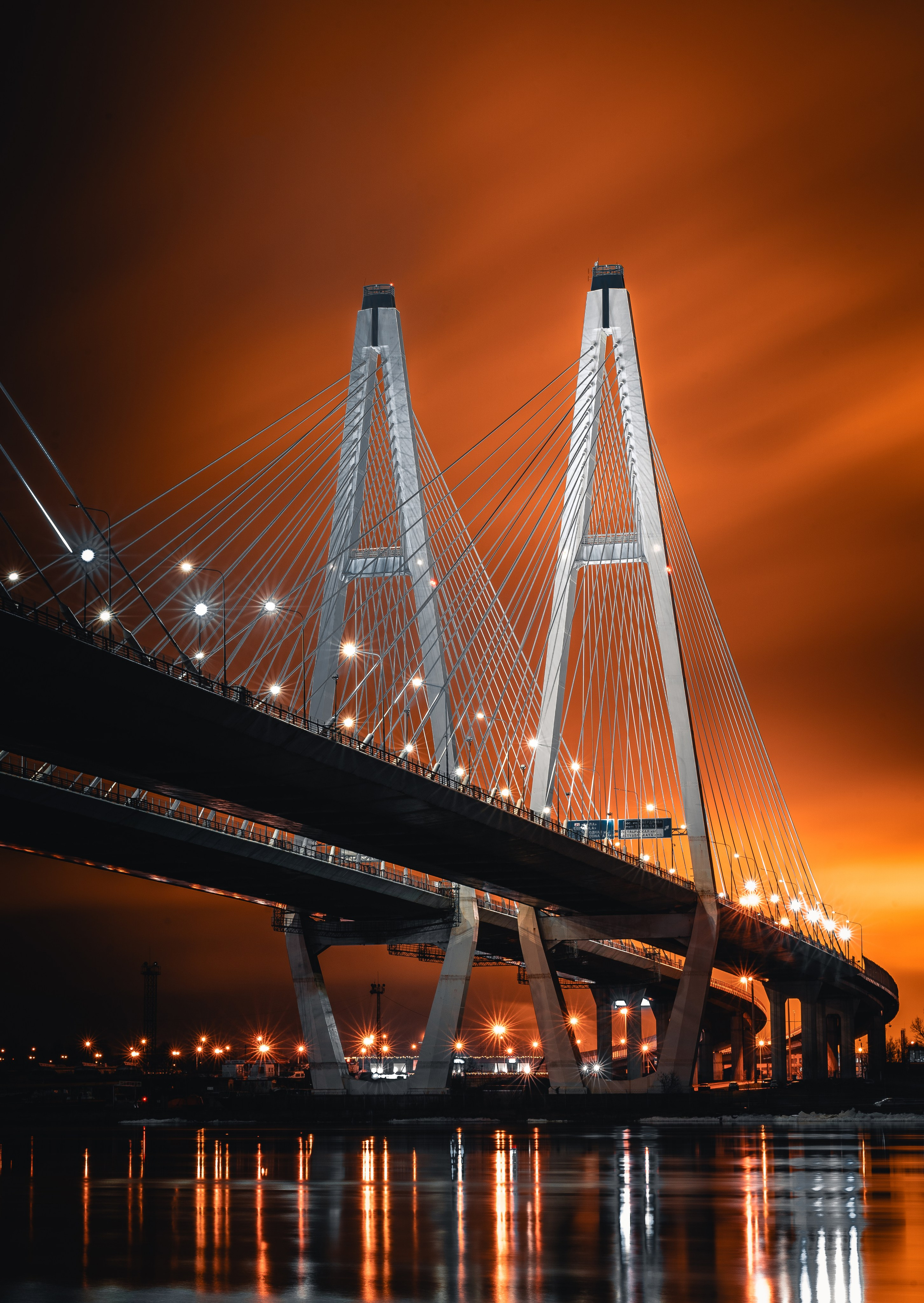 Обуховский мост через  Неву в Санкт-Петербурге ночью, светящиеся опоры и оранжевое небо, атмосферный городской пейзаж, фото Евгений Мальцев.