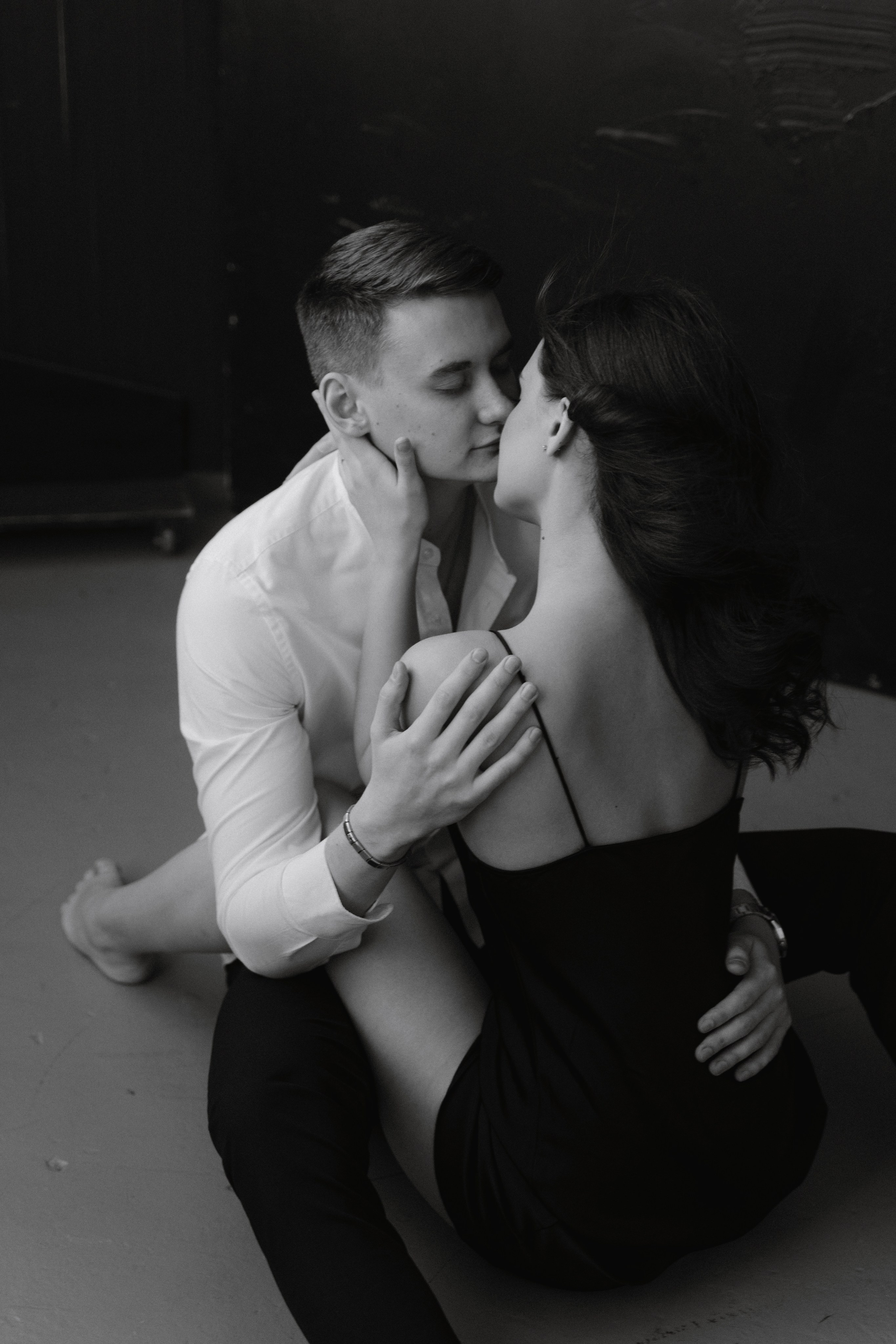 Пара сидит ну полу фотостудии и обнимается. Волосы девушки развиваются от вентилятора.