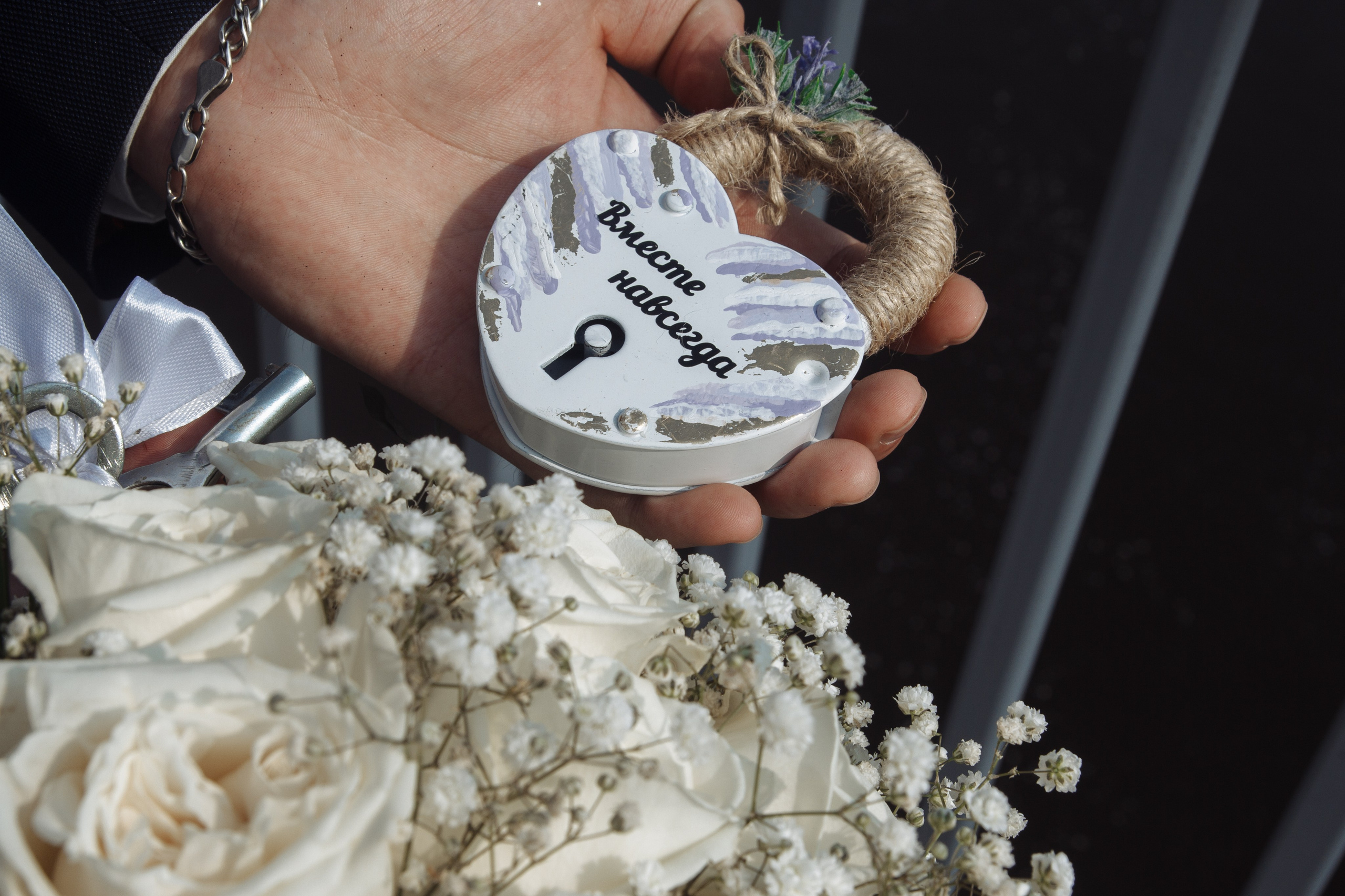 Крупный план рук жениха с бутоньеркой и часами, держит значок с надписью «Жених».