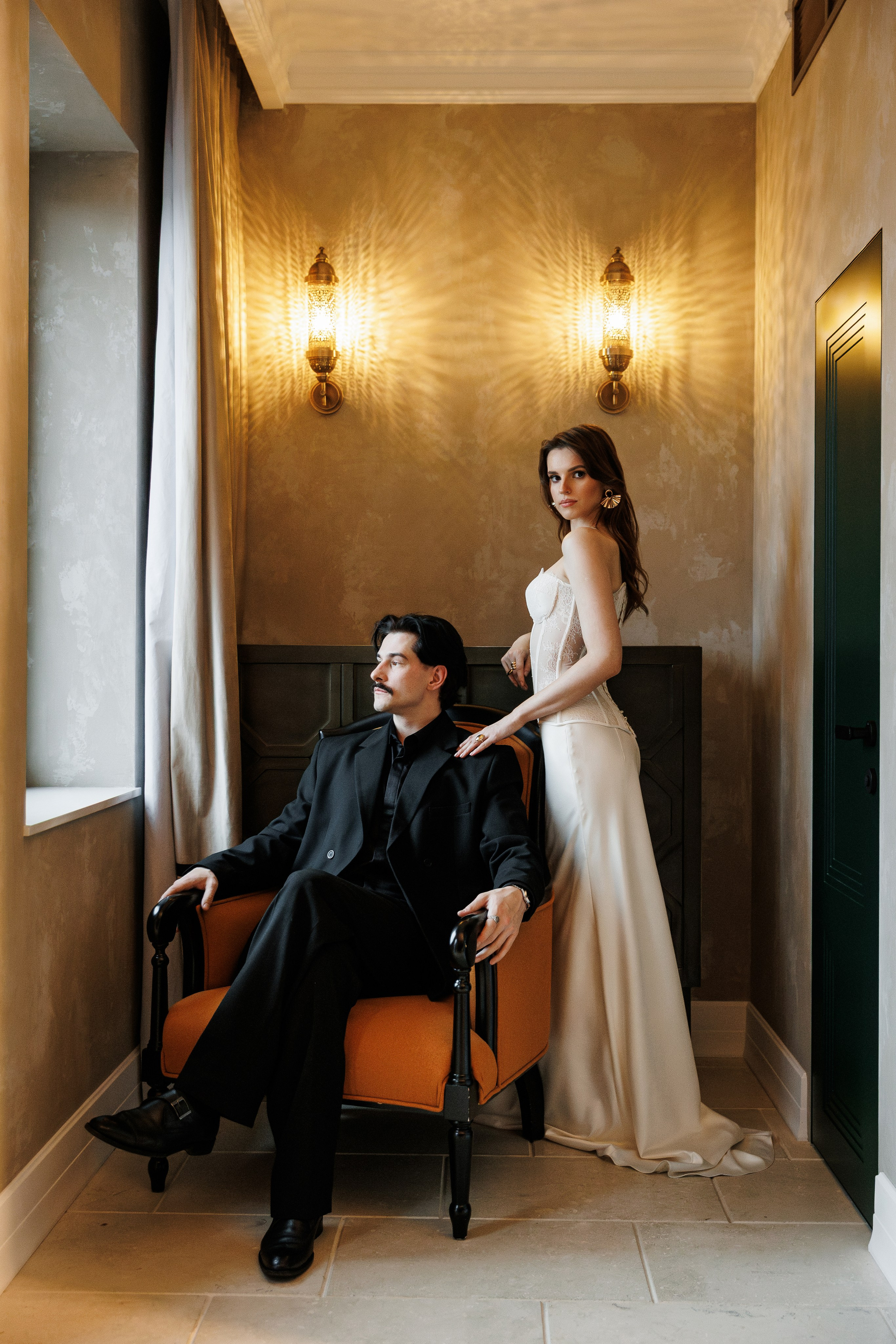 Свадебный фотограф в Минске. Репортажная свадебная фотография пары в отеле, жених сидит, а невеста стоит рядом в Беларуси