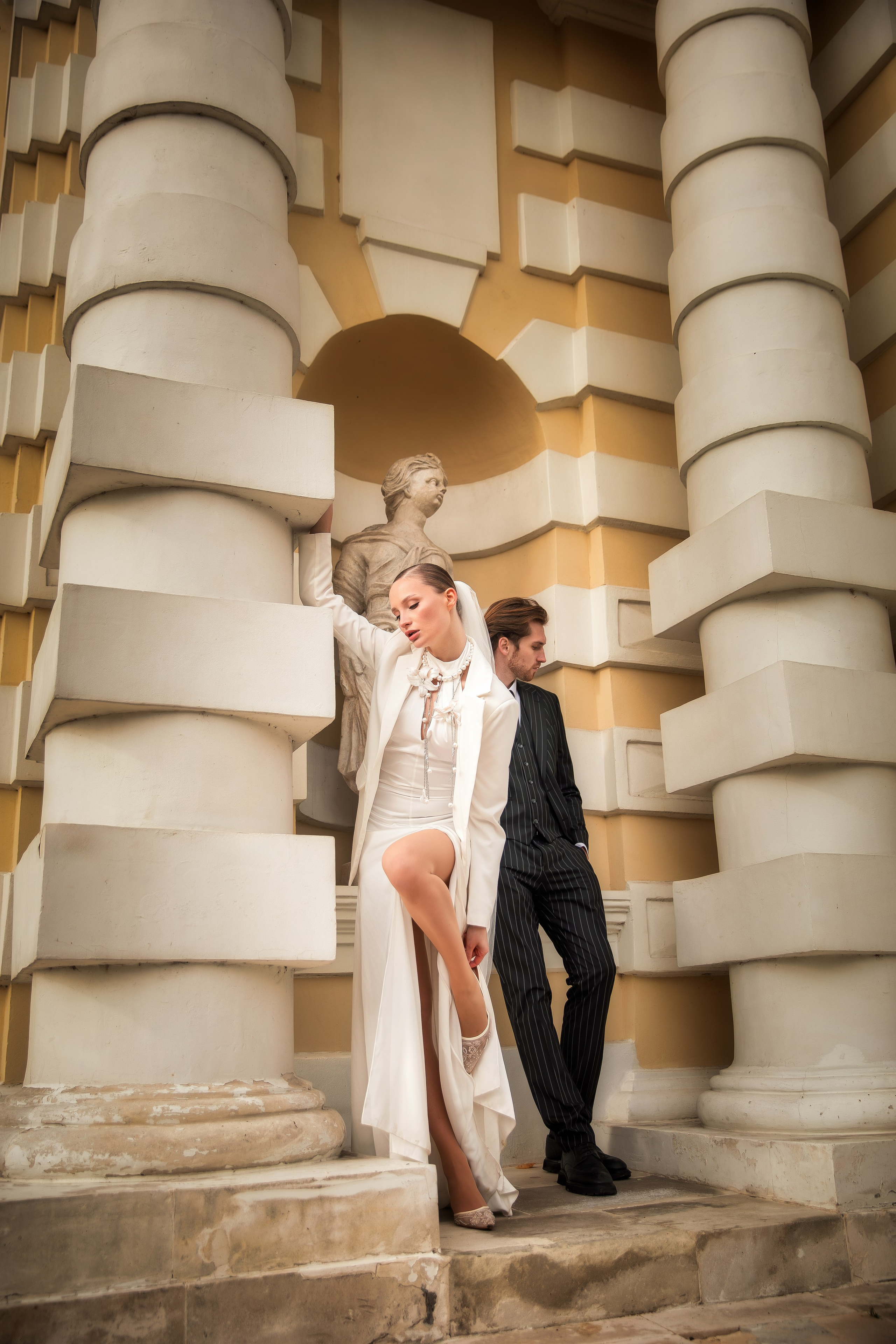 Свадебная пара у колонн усадьбы Кусково, невеста в белом платье и скульптура на заднем плане.