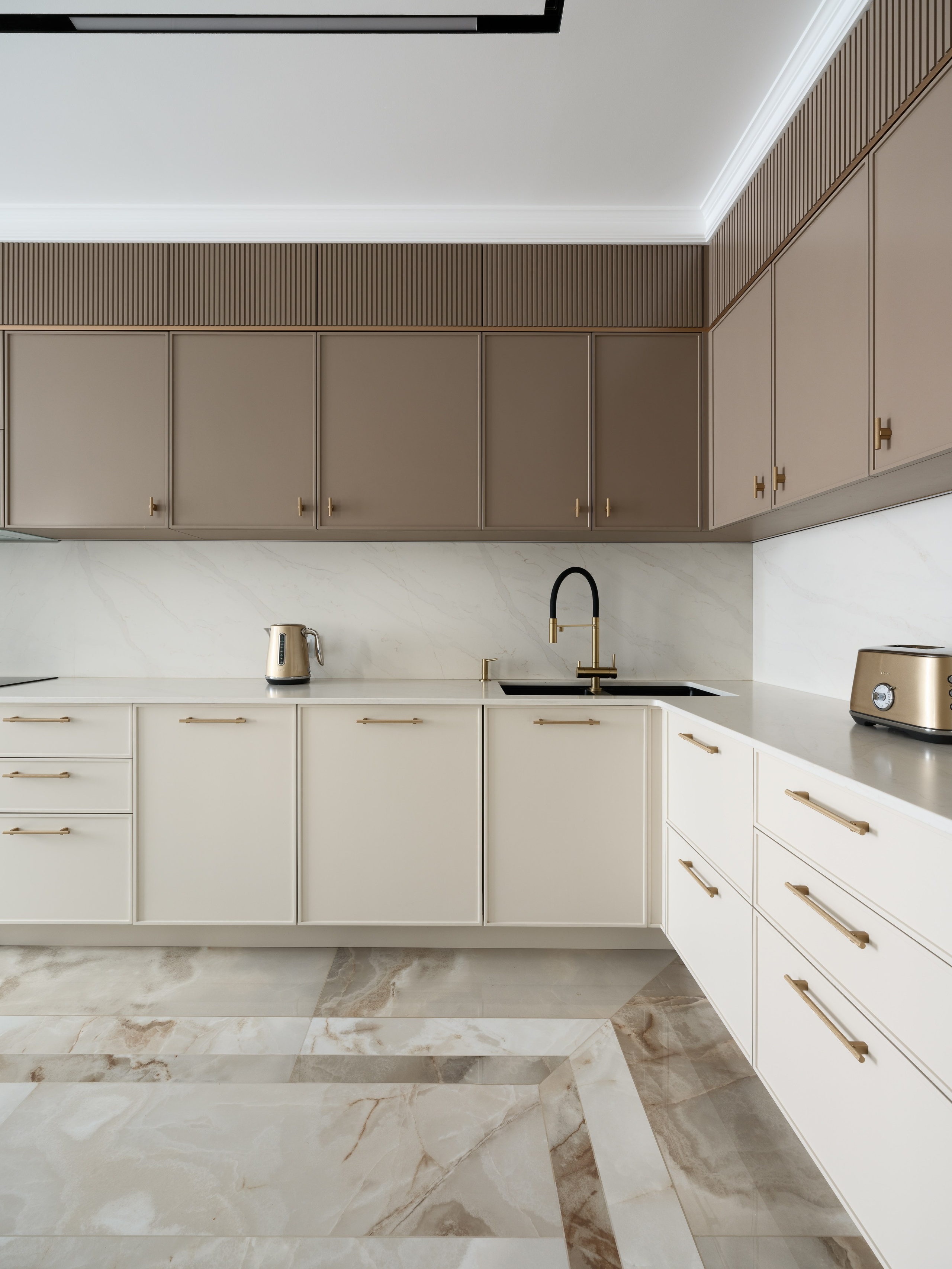 Современная кухня в светло-бежевых и кофейных тонах с матовыми фасадами без лишнего декора, акцентной фурнитурой золотого оттенка и эффектным мраморным полом с геометрическим рисунком, выполненная по проекту дизайнера Евгении Ермошиной и запечатлённая фотографом Сергеем Денисенко.
