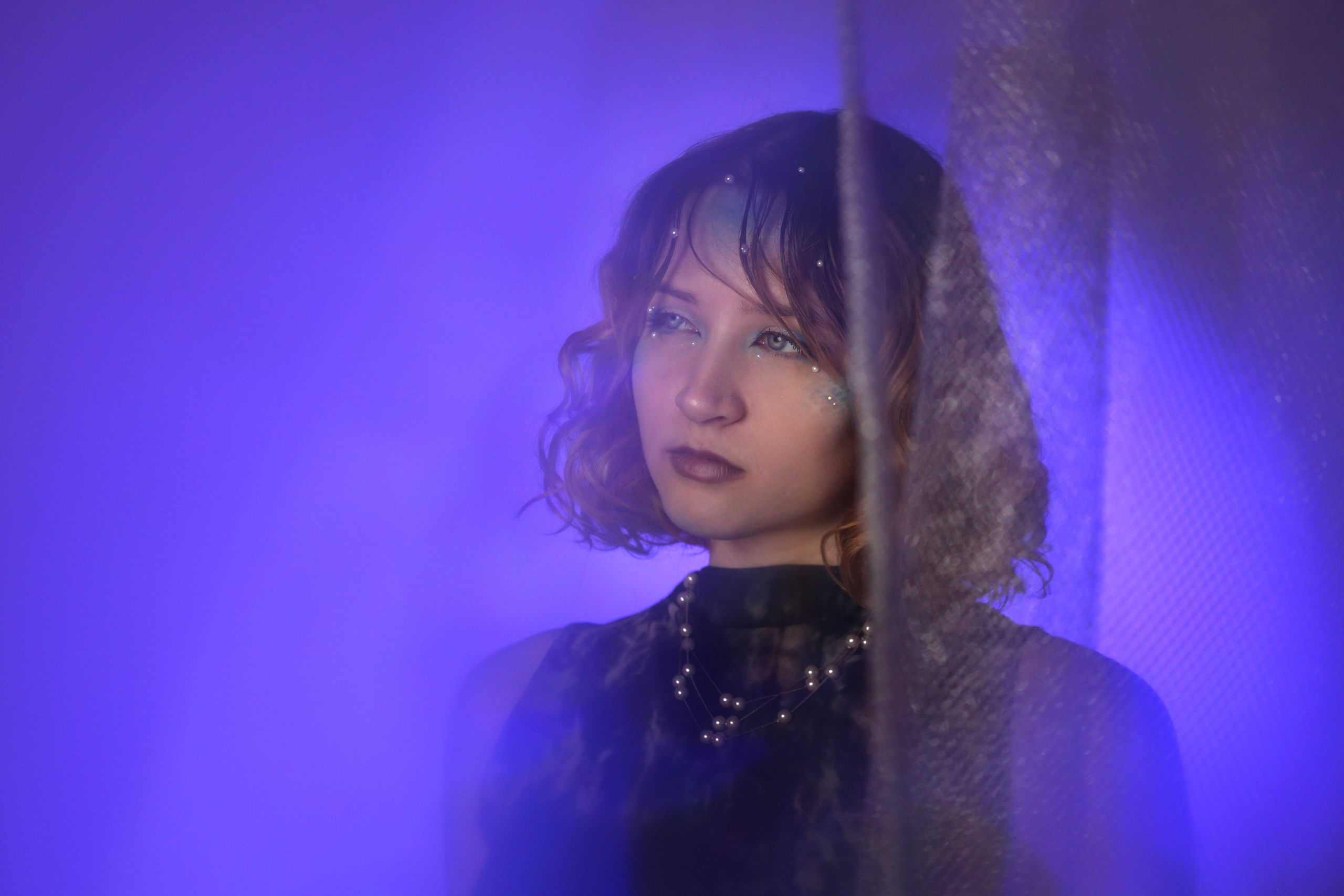 Портрет из фотосессии «Ундина»: девушка в черном платье в профиль на фоне фиолетового света