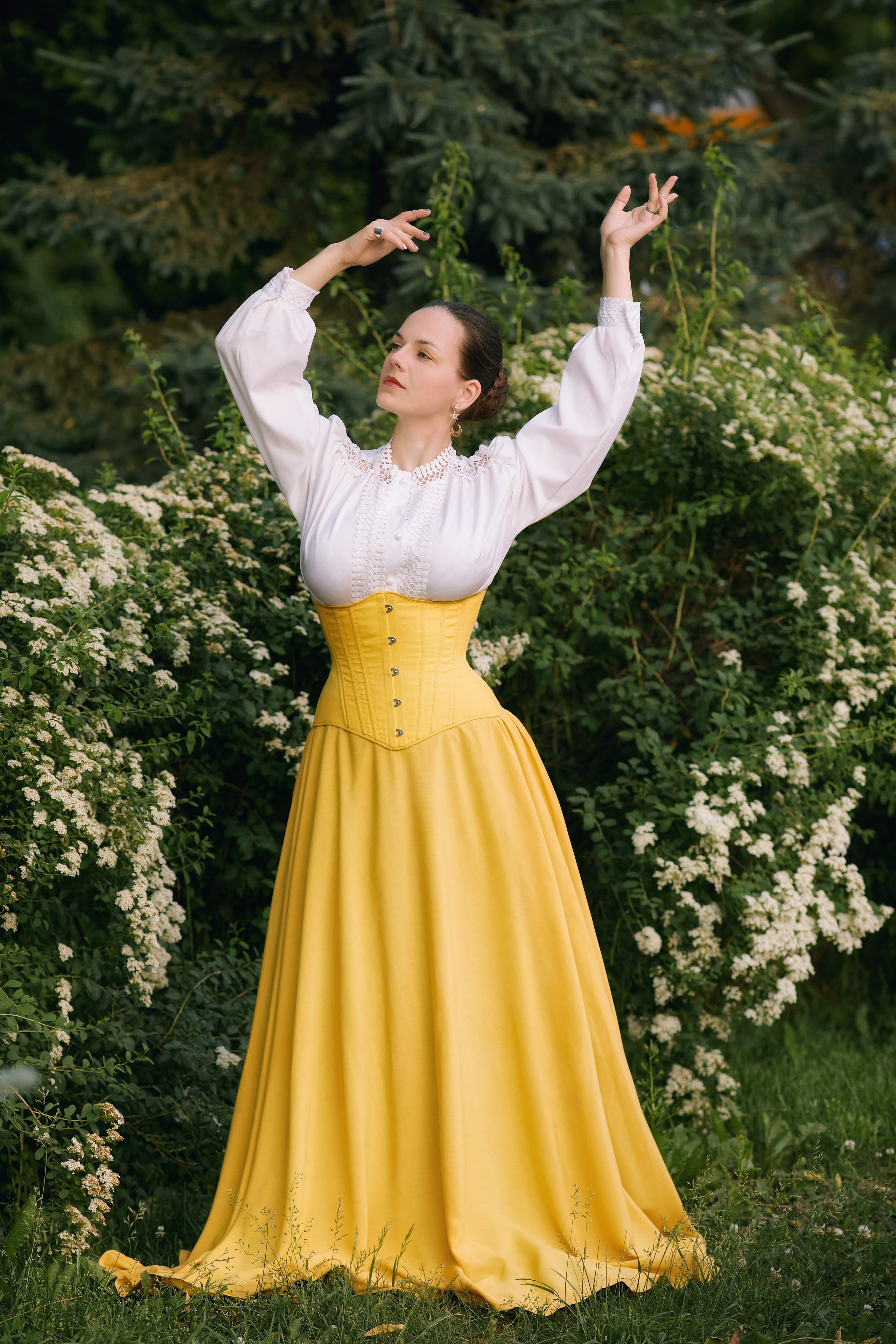 Уличная косплей фотосессия в Находке с женщиной в белой блузке и жёлтом платье, позирующей на фоне цветов и зелени