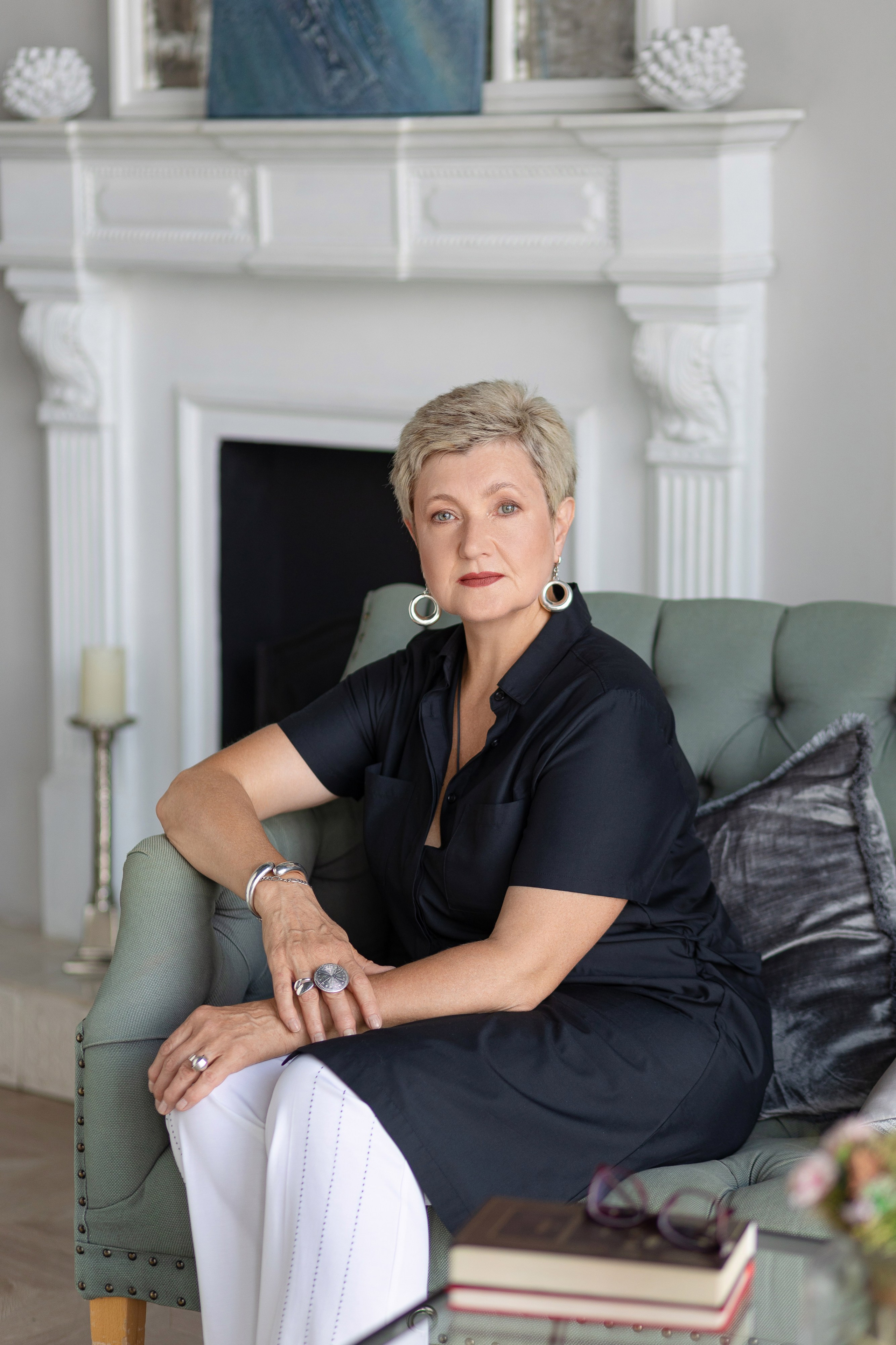 Женщина сидит на диване на фоне камина.Слева на диване подушка.