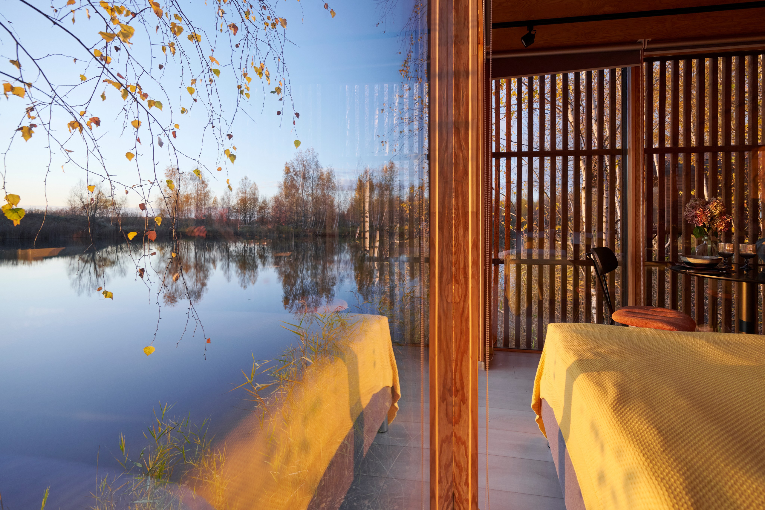 Панорамное окно, отражение озера, деревянные стойки и свет.