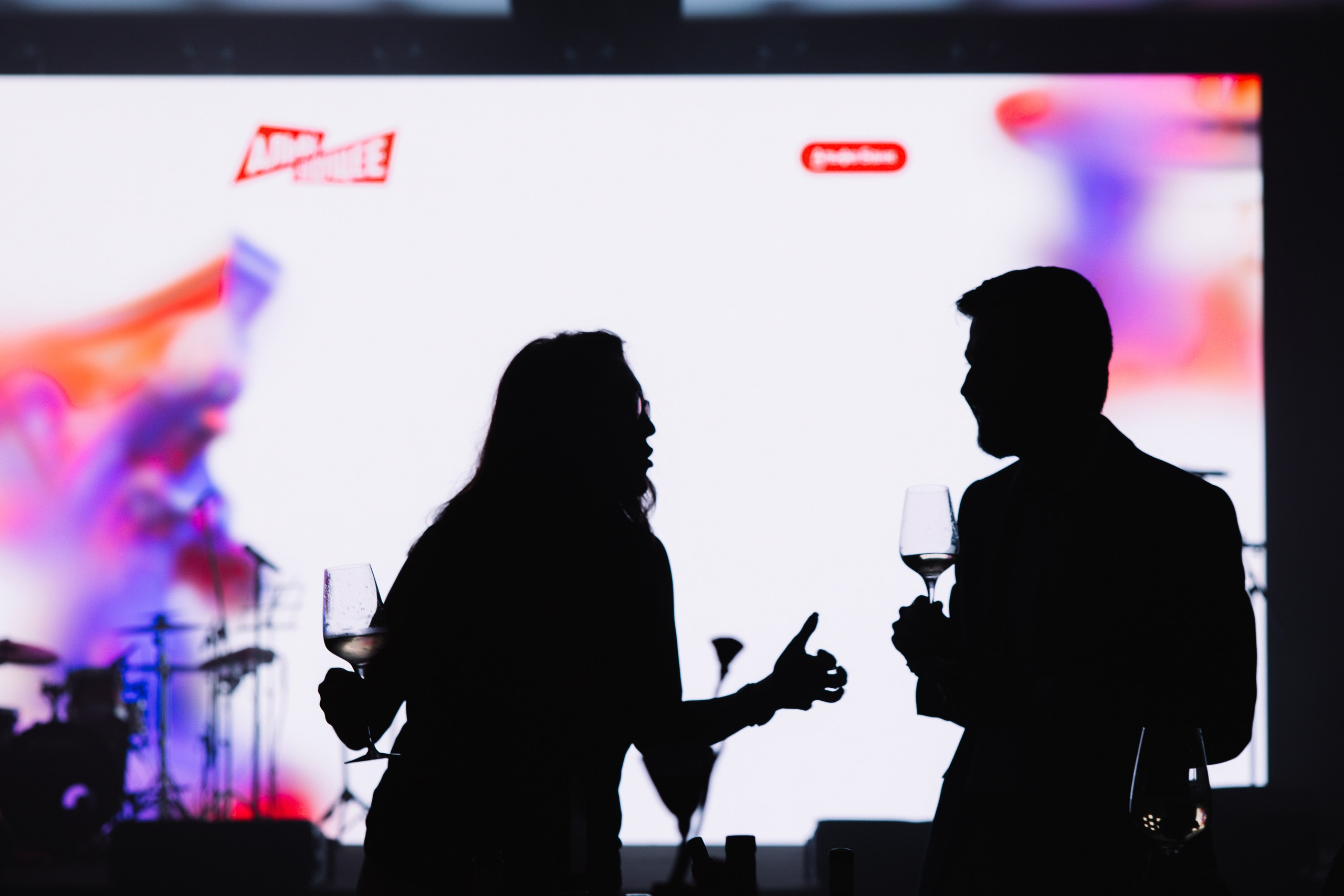 Силуэты: Мужчина и женщина общаются на фоне ярко подсвеченного мультимедийного экрана.