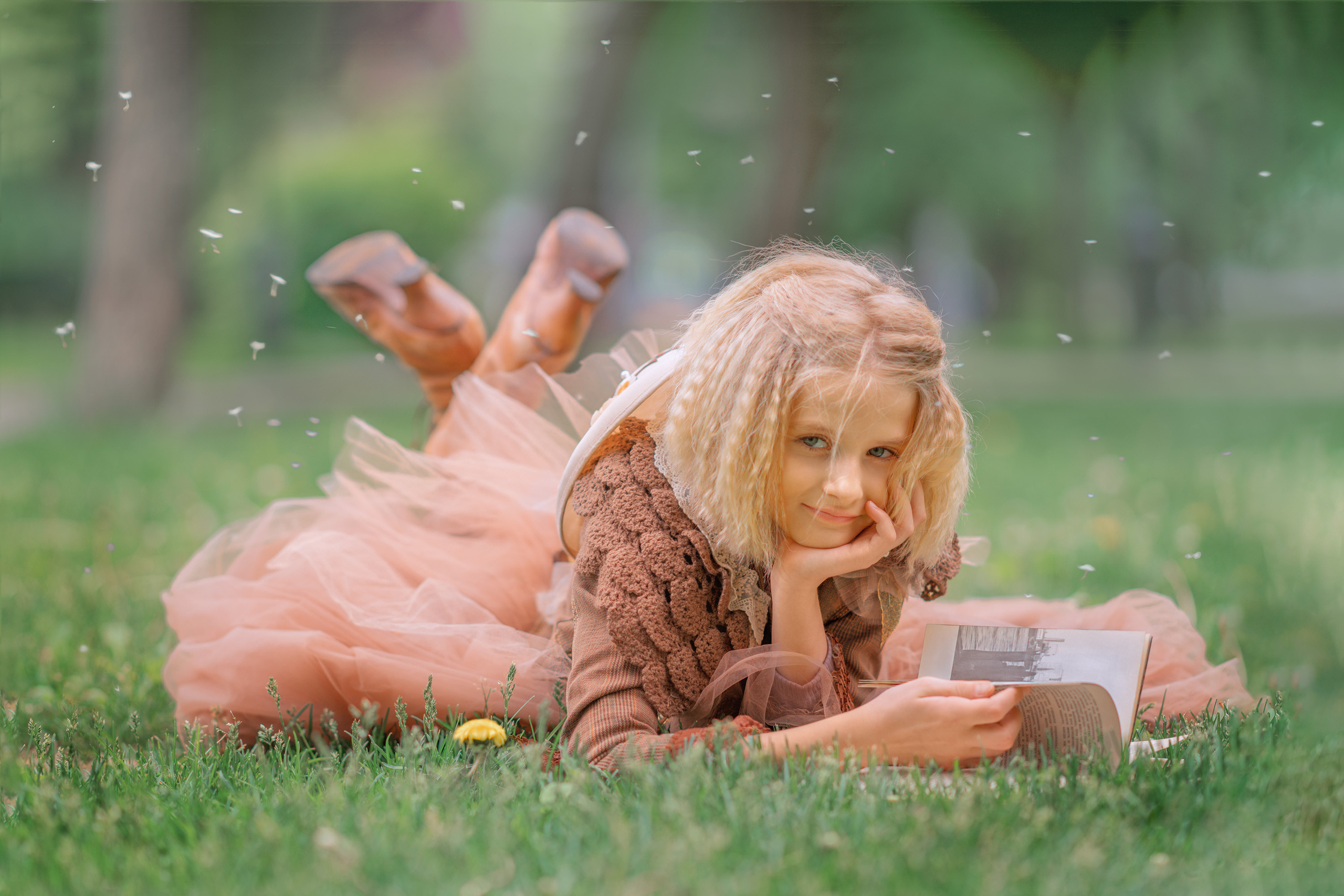 Молодая девушка, подросток в старинном платье читает книгу уперев руку в подбородок лежа на траве