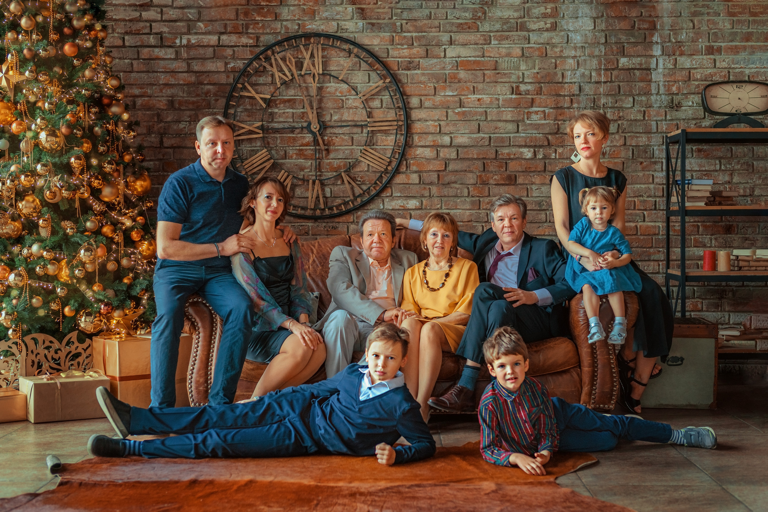 Большая семья сидит на диване на фоне кирпичной стены и новогодней елки