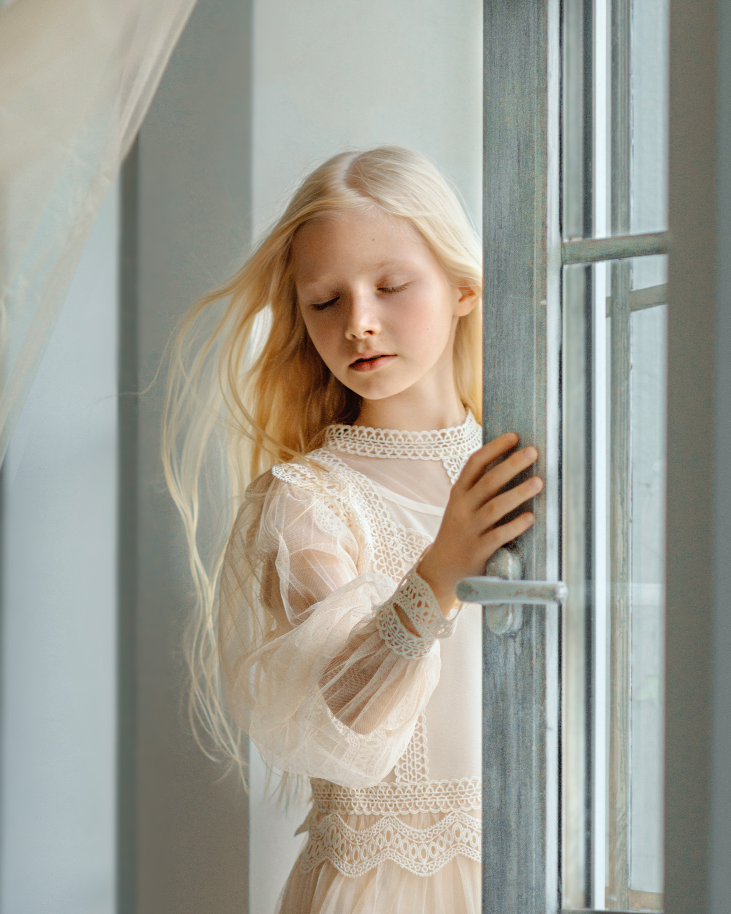 Девочке в лицо дует ветер из раскрытого окна, развиваются волосы