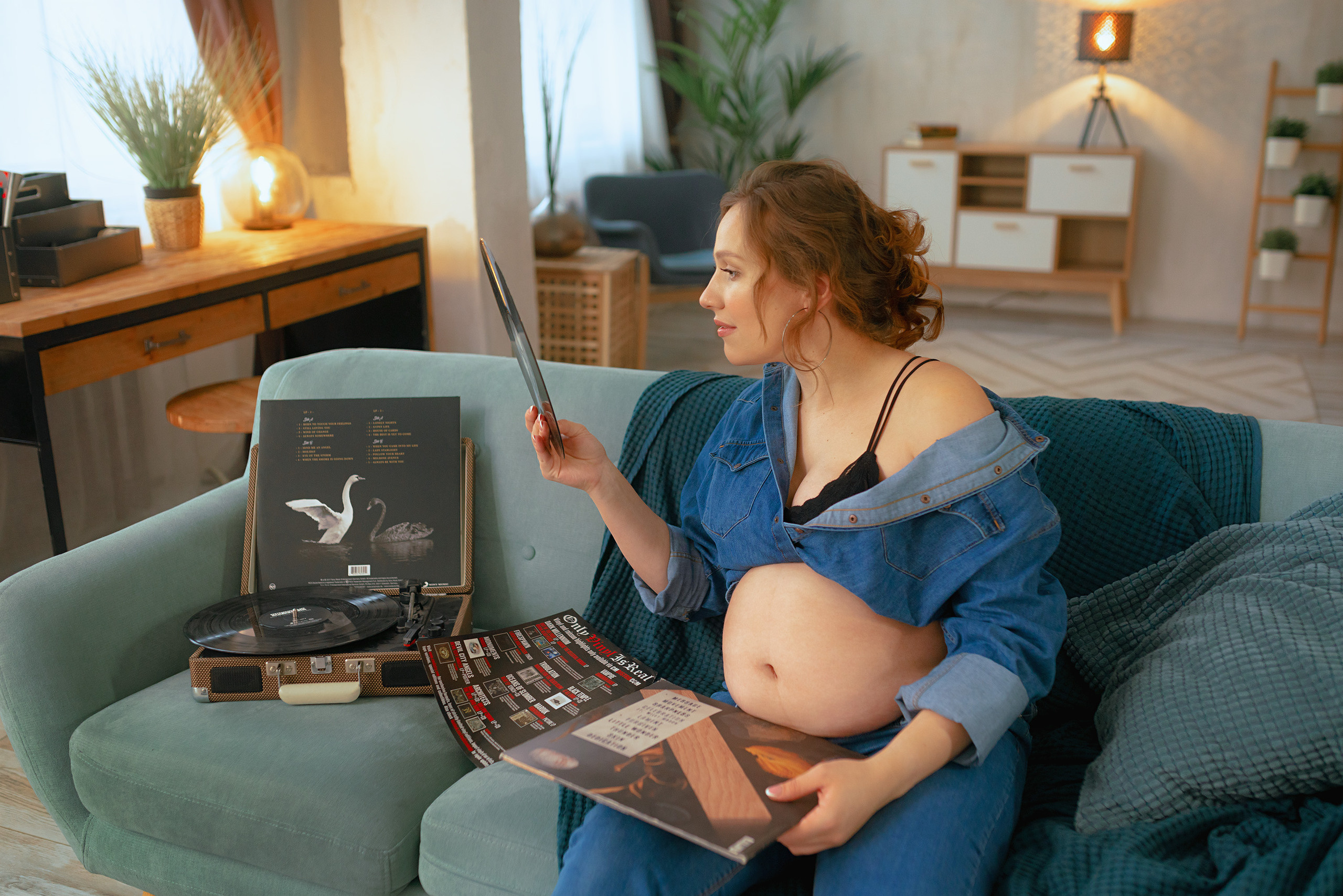 Беременная смотрит на пластинку  сидя на диване в квартире