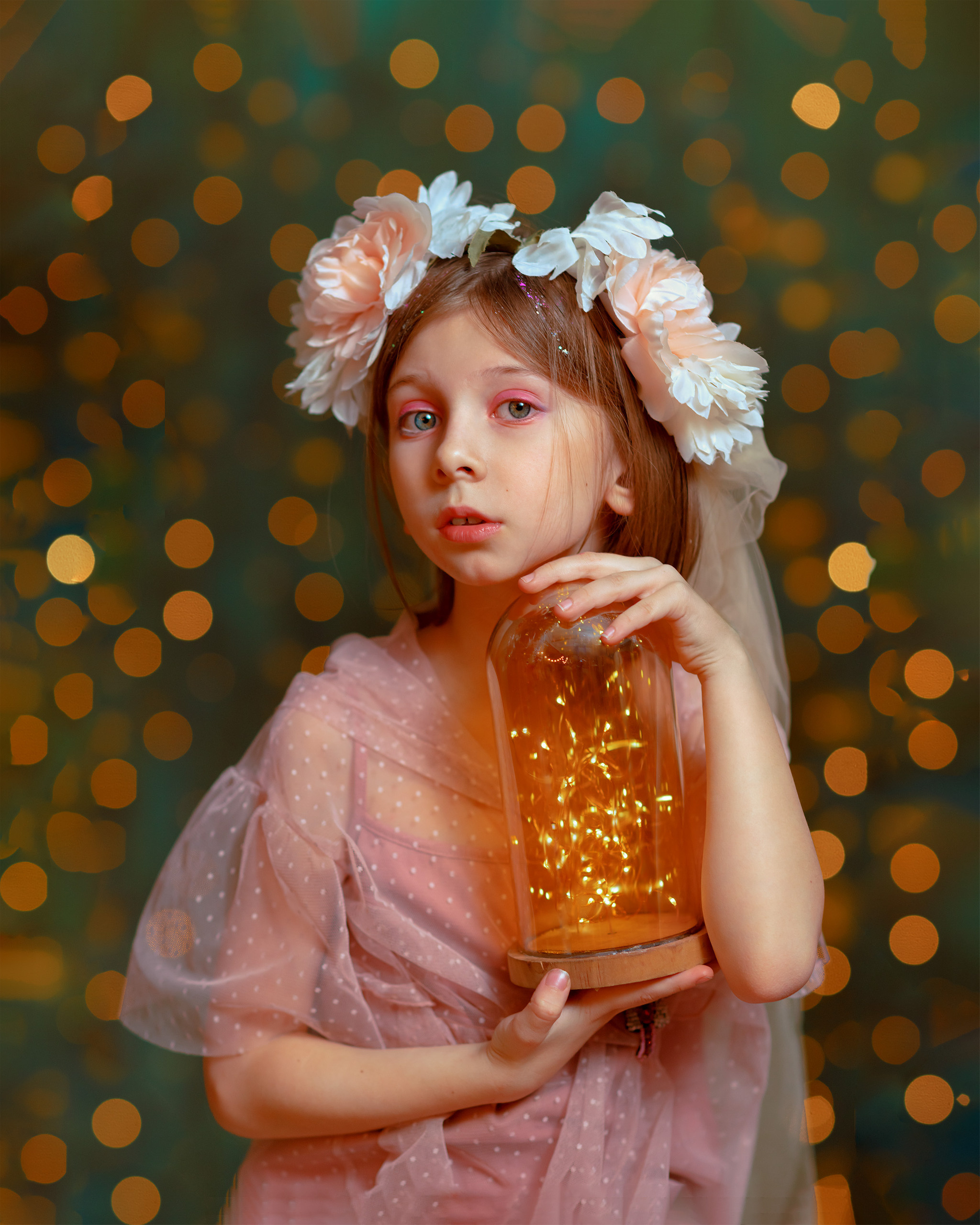 Девочка в сказочном образе с венком на голове и банкой светлячков в руках на фоне огоньков