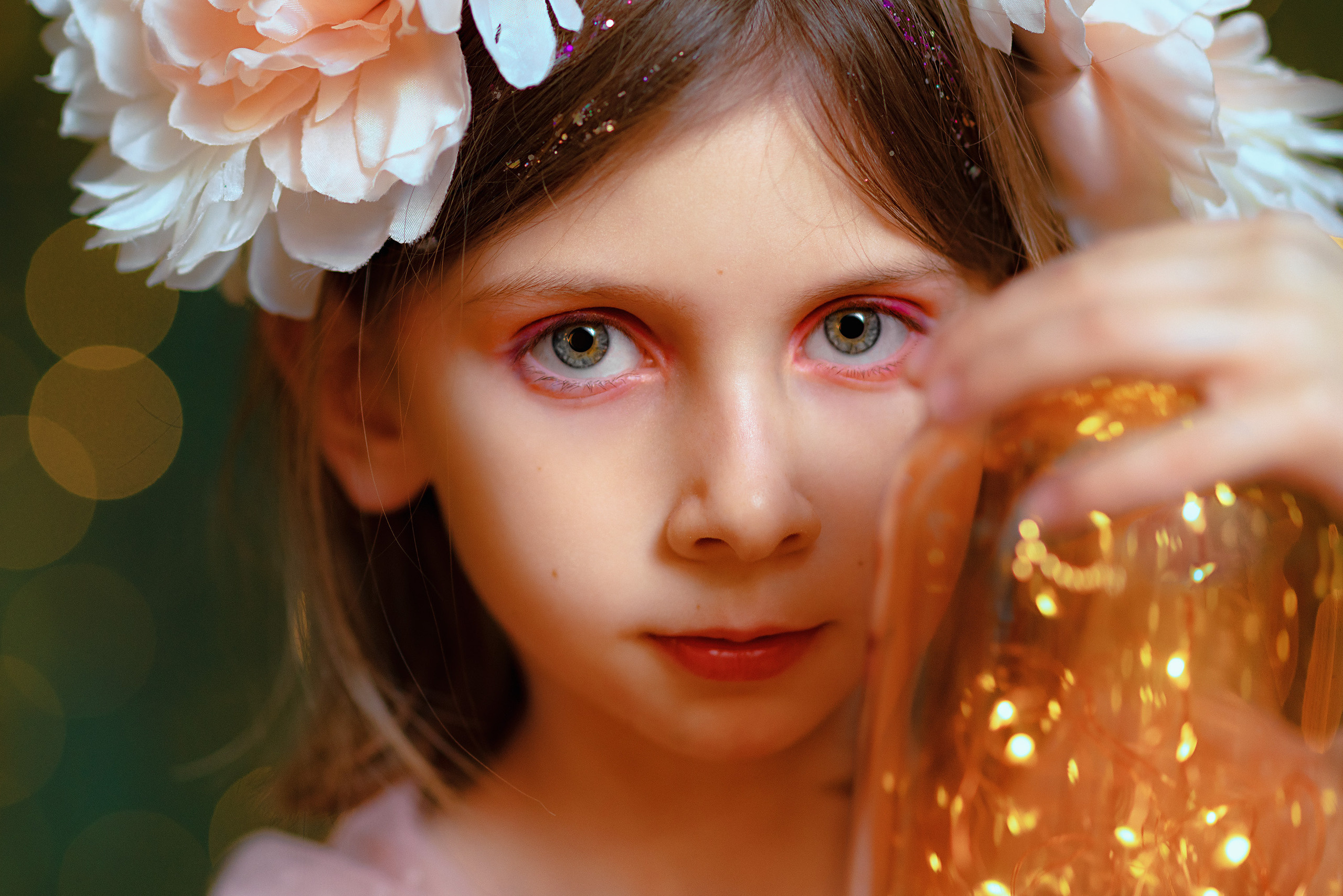 Крупный портрет девочки в сказочном образе с венком на голове и банкой светлячков в руках на фоне огоньков