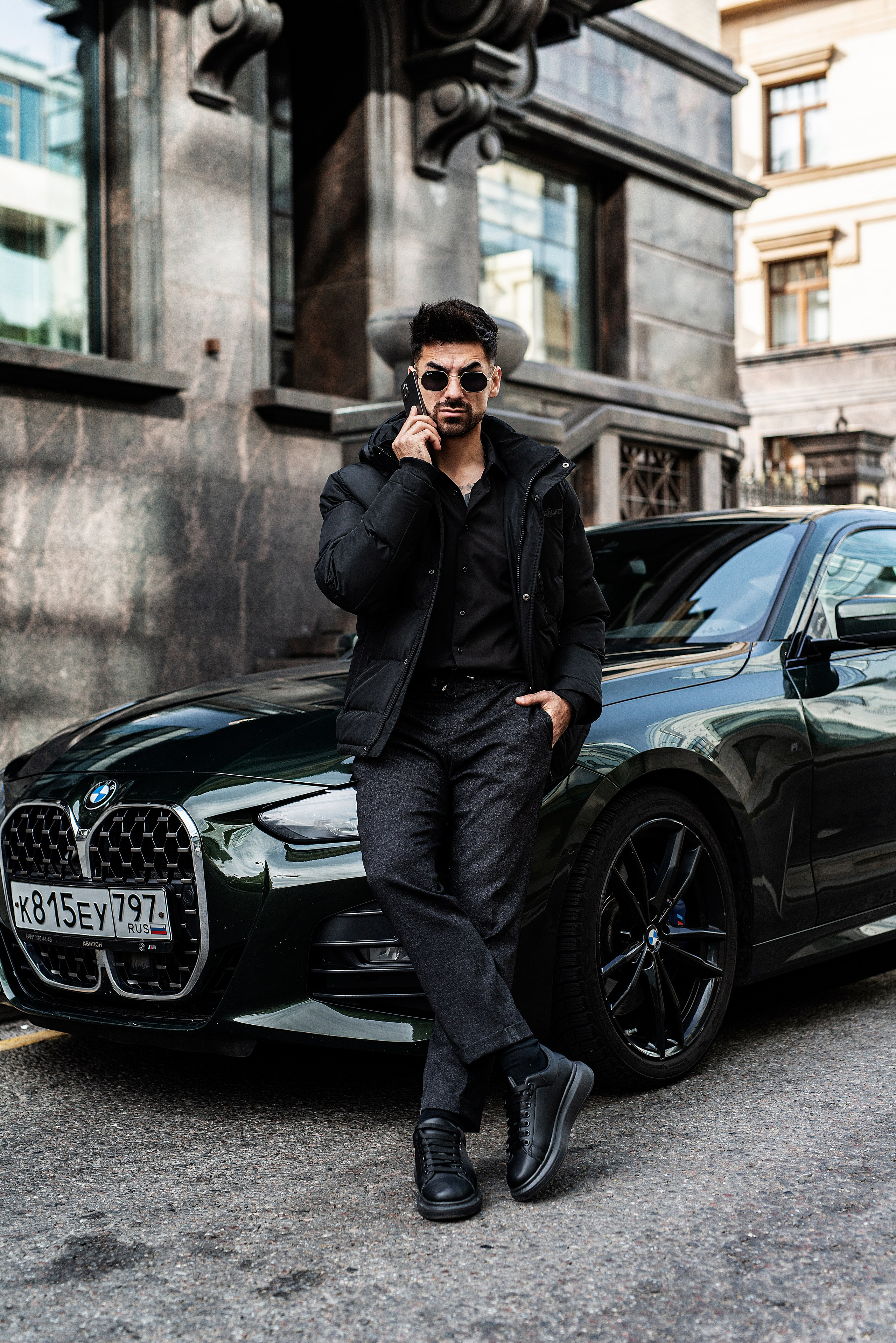 Стильный мужчина позирует на камеру на фоне BMW, фотография в полный рост