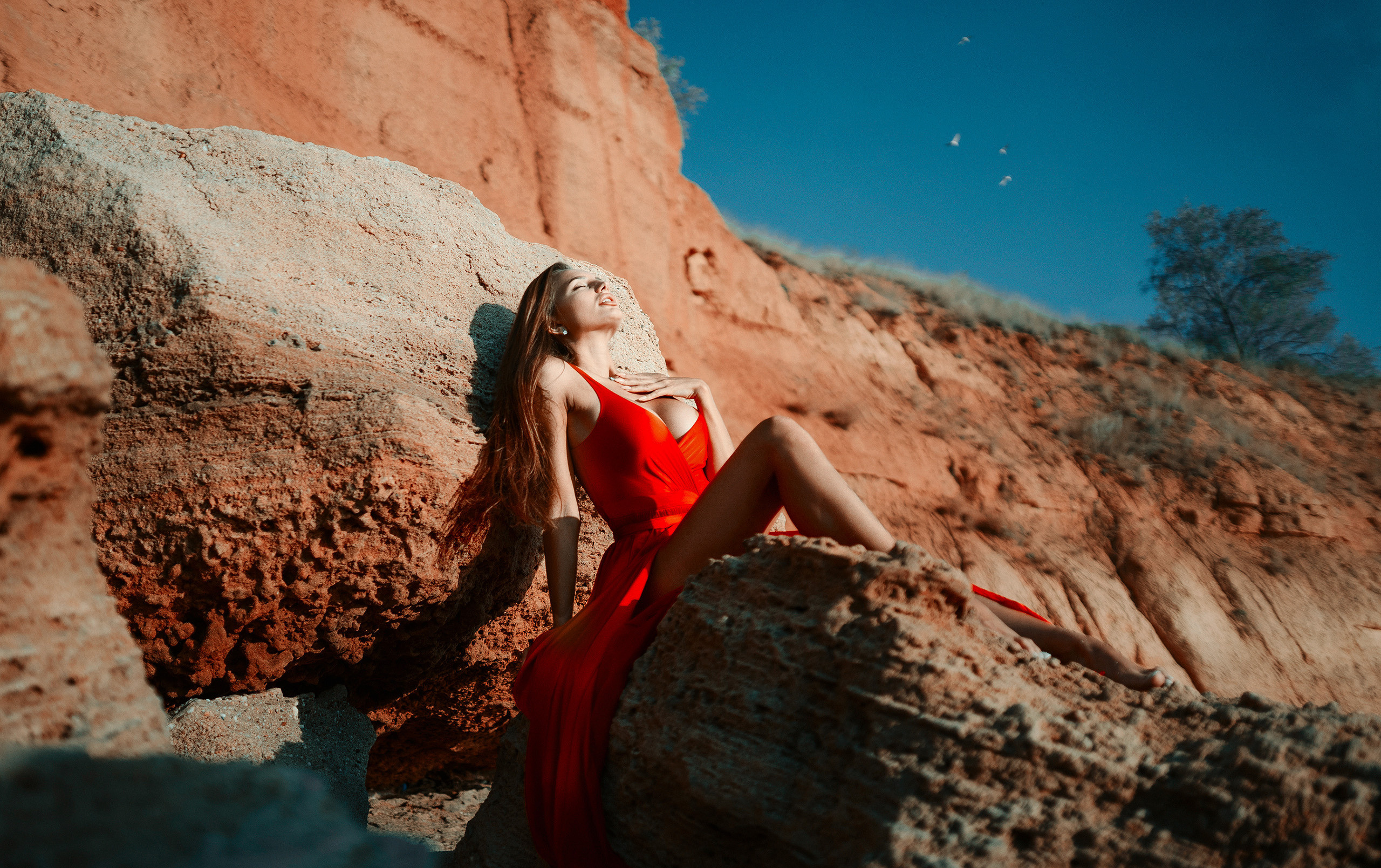 Девушка в красном платье на берегу моря сидит на камне