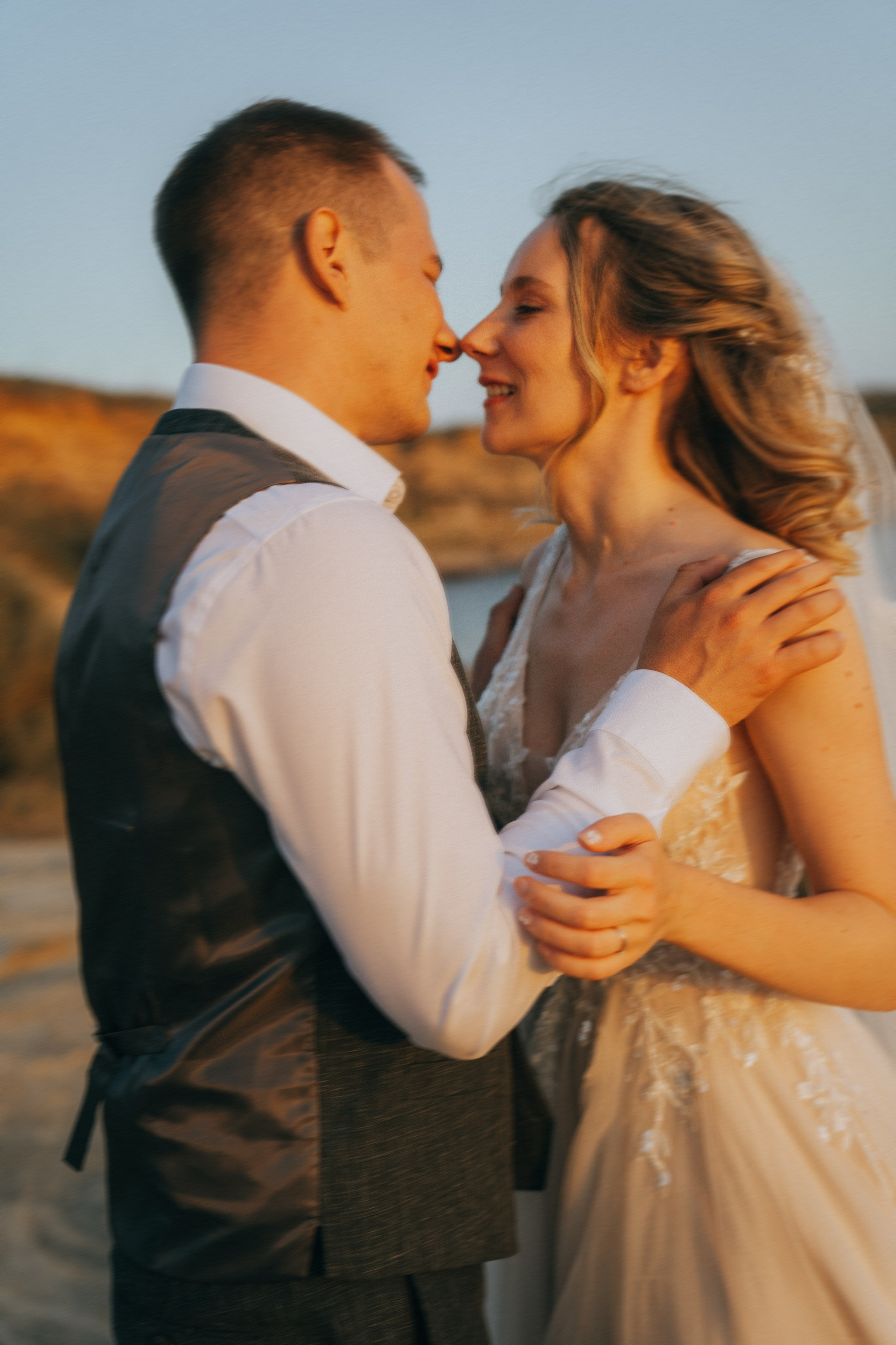 Счастливая пара жених и невеста целуется на фоне волн  скал и заката у океана.