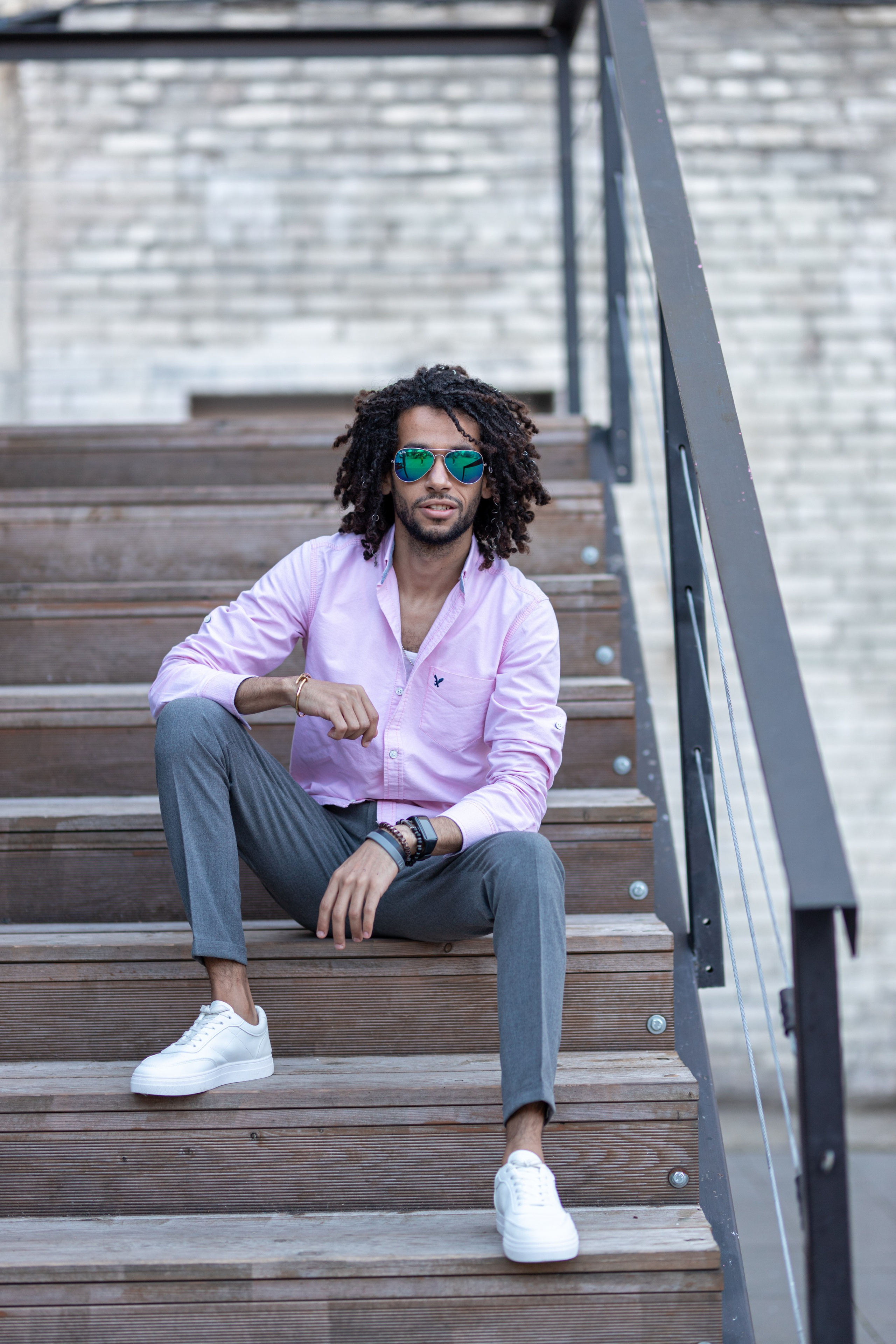 Темнокожий парень в брюках и розовой рубашке сидит на лестнице