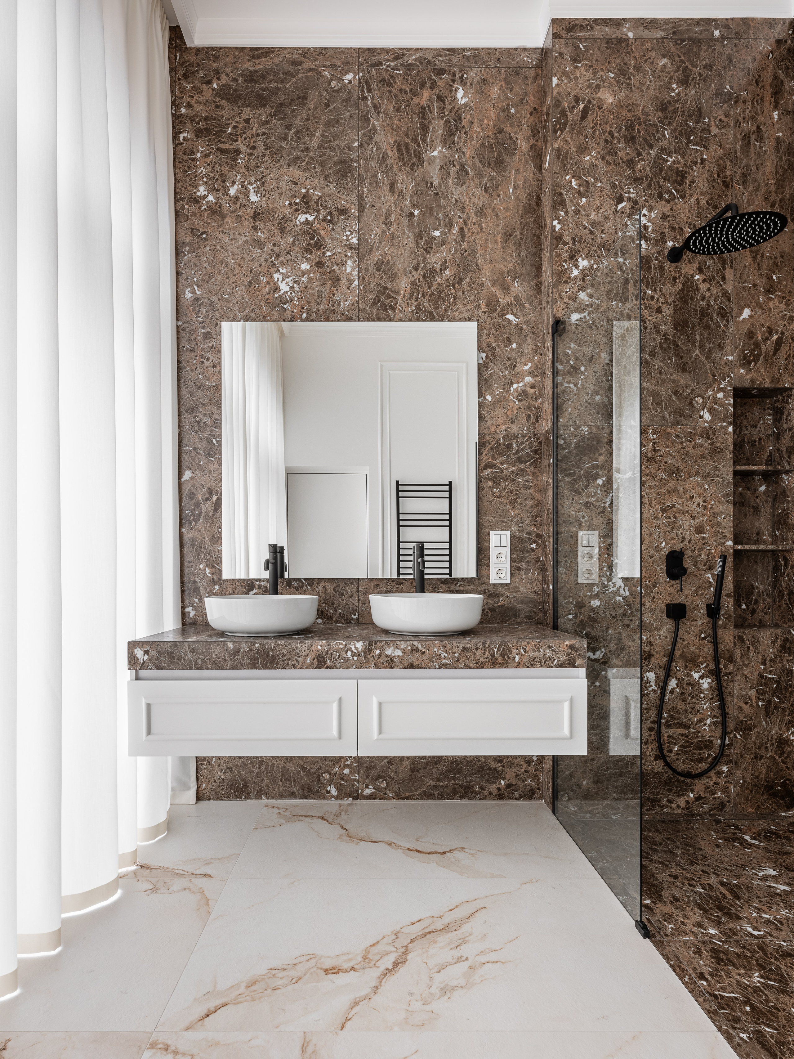 Роскошная ванная комната с отделкой коричневым мрамором, двумя раковинами-чашами на белой тумбе, стеклянной душевой кабиной и черной сантехникой, оформленная дизайнером Василиссой Бачевой, стилистом Натальей Якушевой и снятая фотографом Сергеем Денисенко.