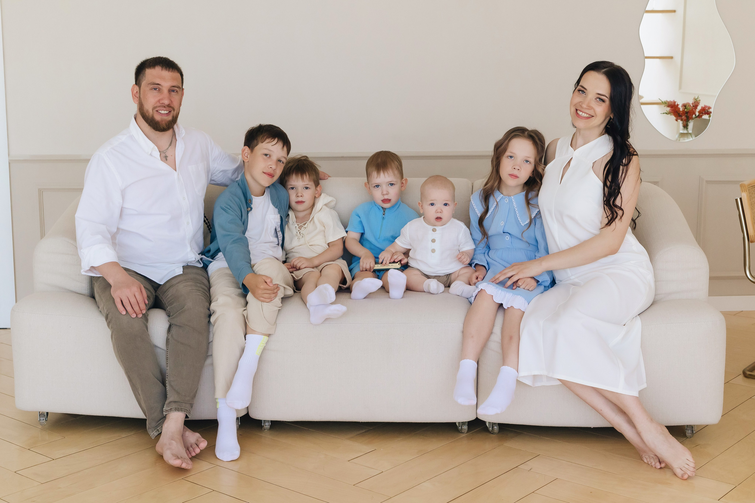 Семья из семи человек сидит на диване, мама и папа по краям, их дети между ними