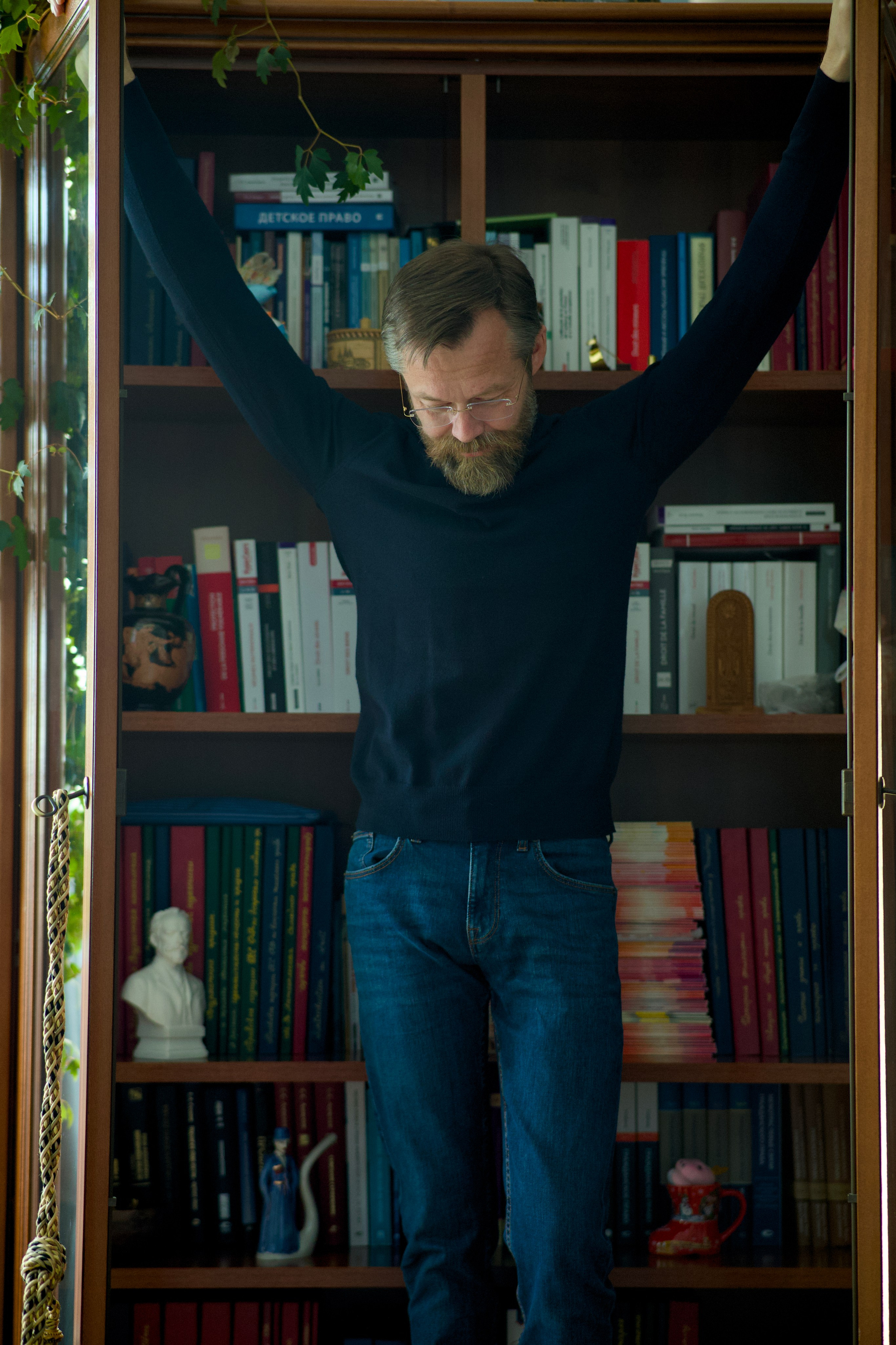 Юрист в очках ищет книгу на верхней полке. Снимок в профиль. Корпоративная фотография рабочих будней от Ильи Антропова, Екатеринбург.