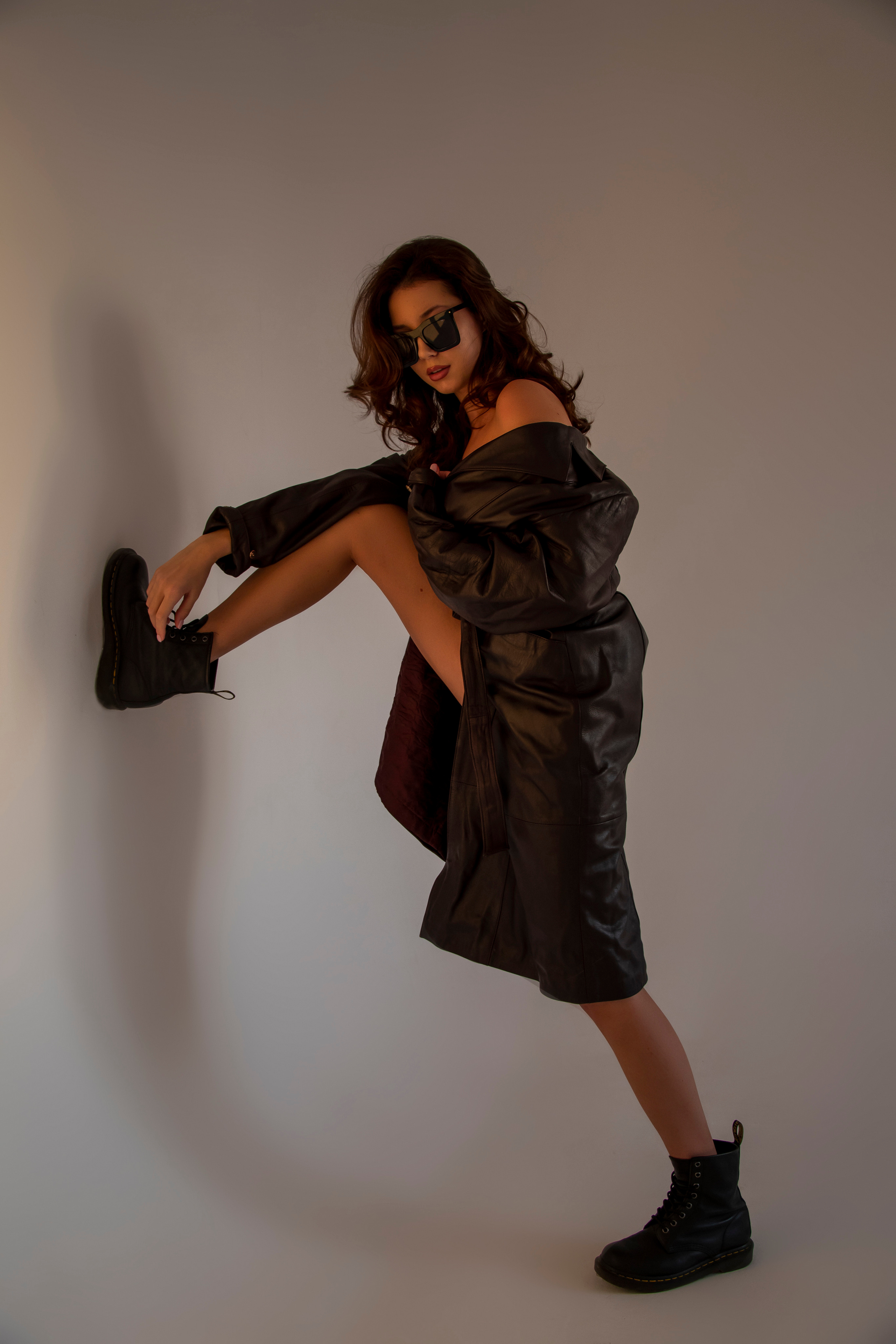 Красивая девушка в кожаном плаще на голое тело на закате в студии циклораме модельный тест фотоссесия циклорама