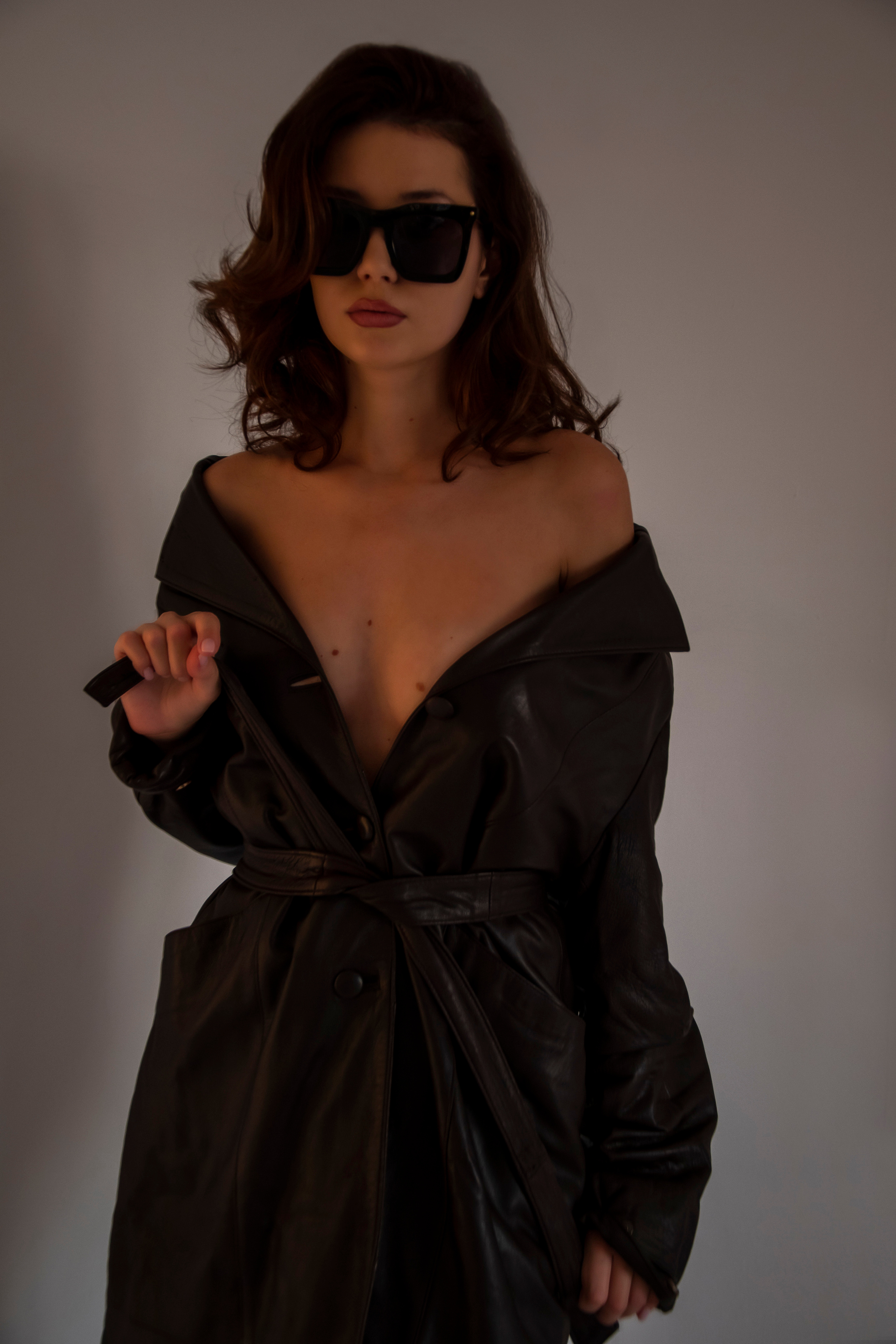 Красивая девушка в кожаном плаще на голое тело на закате в студии циклораме модельный тест фотоссесия циклорама