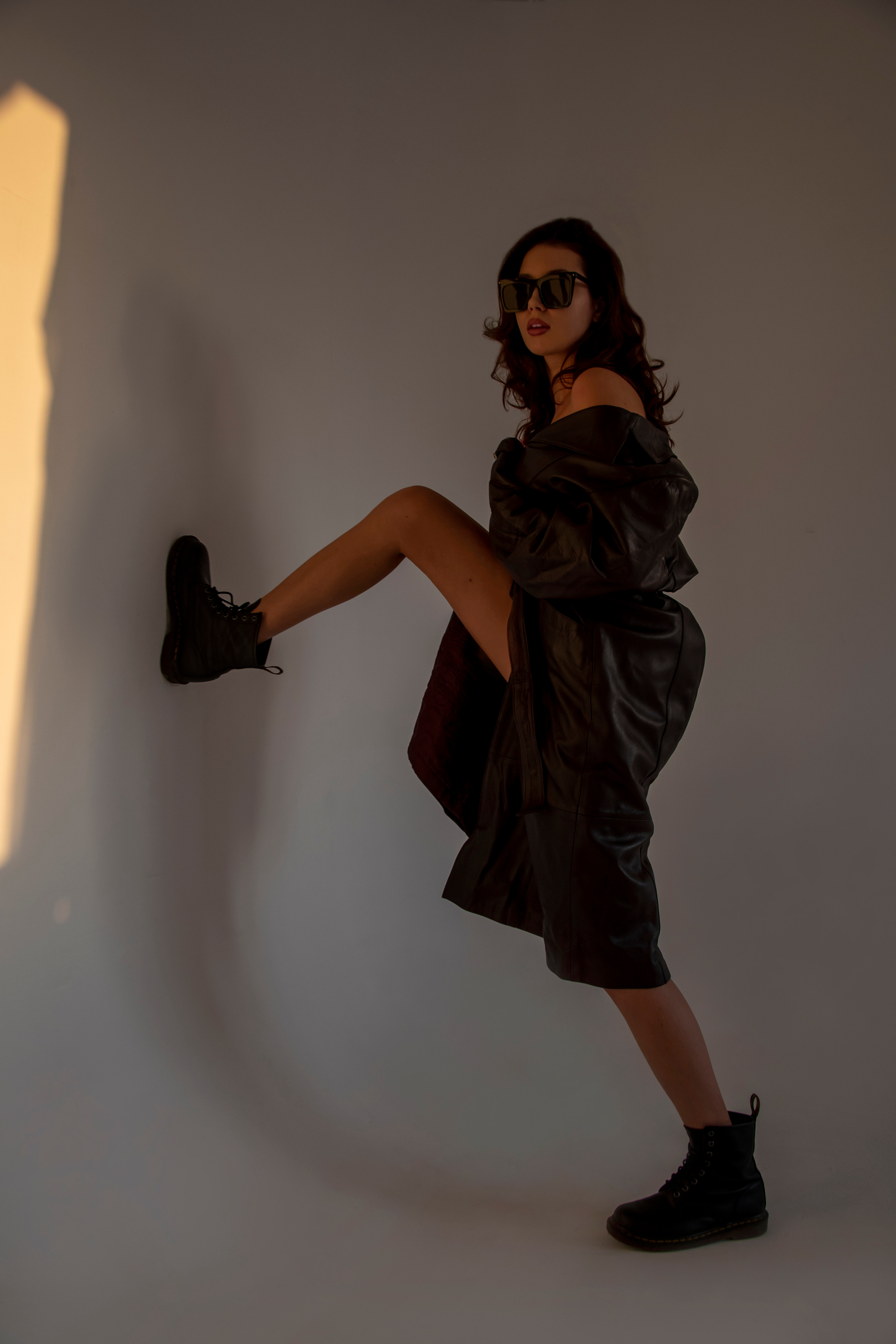 Красивая девушка в кожаном плаще на голое тело на закате в студии циклораме модельный тест фотоссесия циклорама