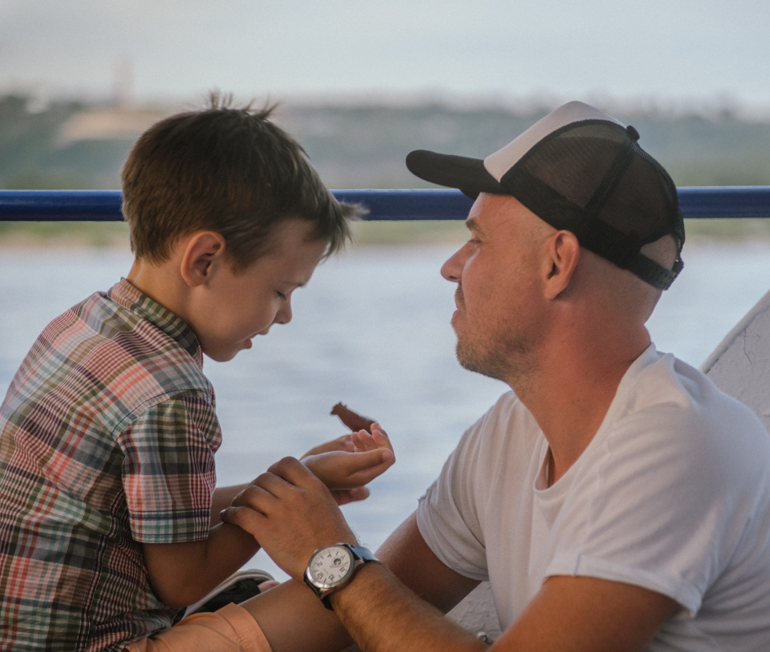 Мальчик вручает отцу что-то маленькое, оба счастливы — тёплый момент на фоне воды.