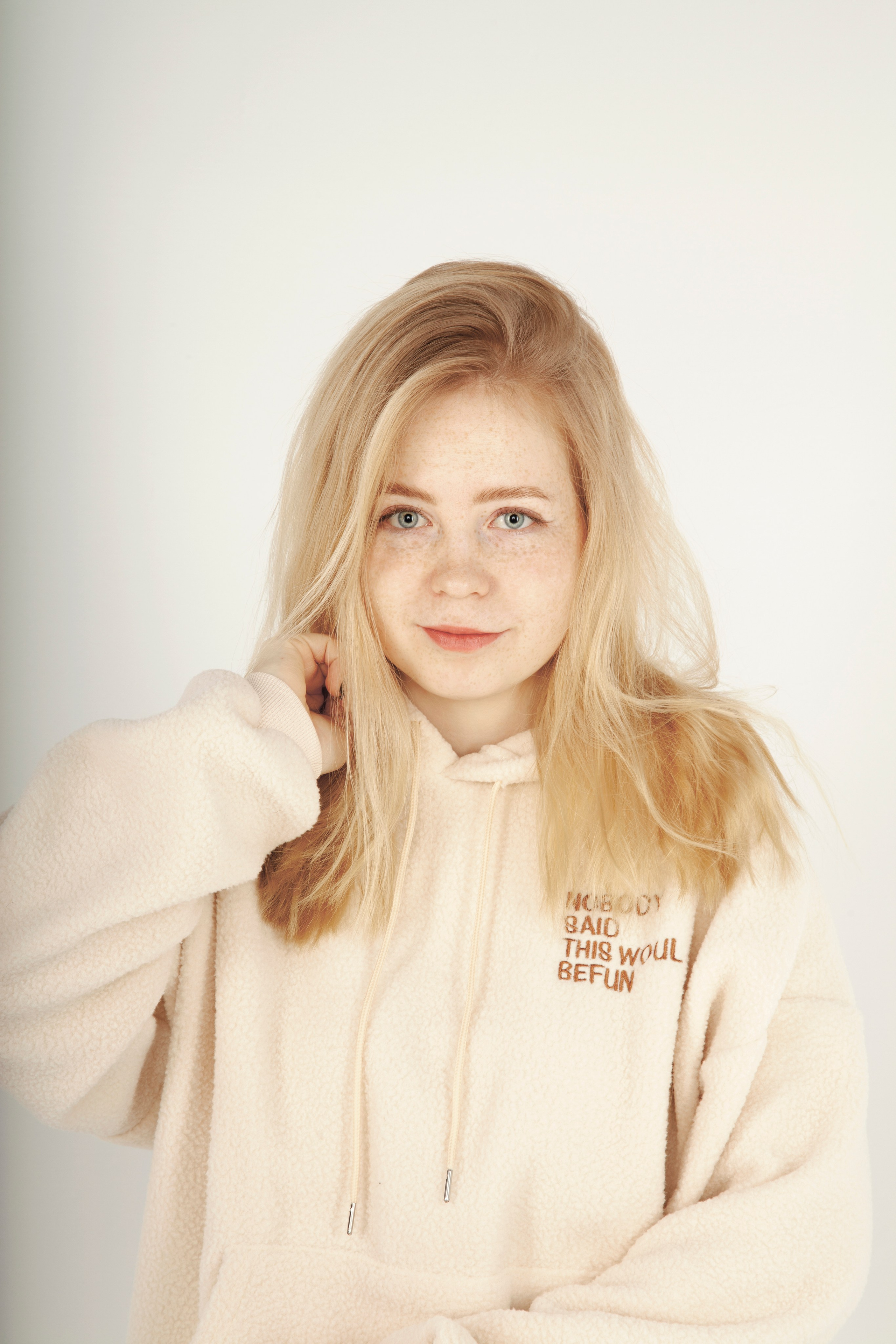 Портрет светловолосой и голубоглазой девушки с веснушками. В светлой одежде на белом фоне.