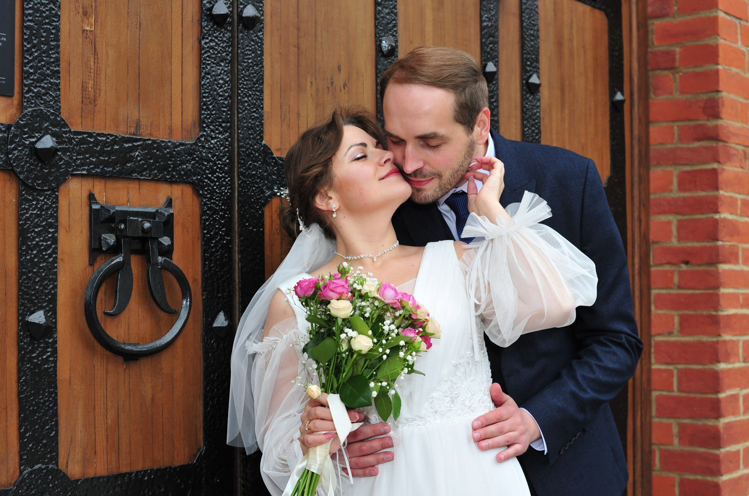 Свадьба в Царицыно пасмурным летним днем, поцелуй новобрачных на фоне старинной деревянной двери 