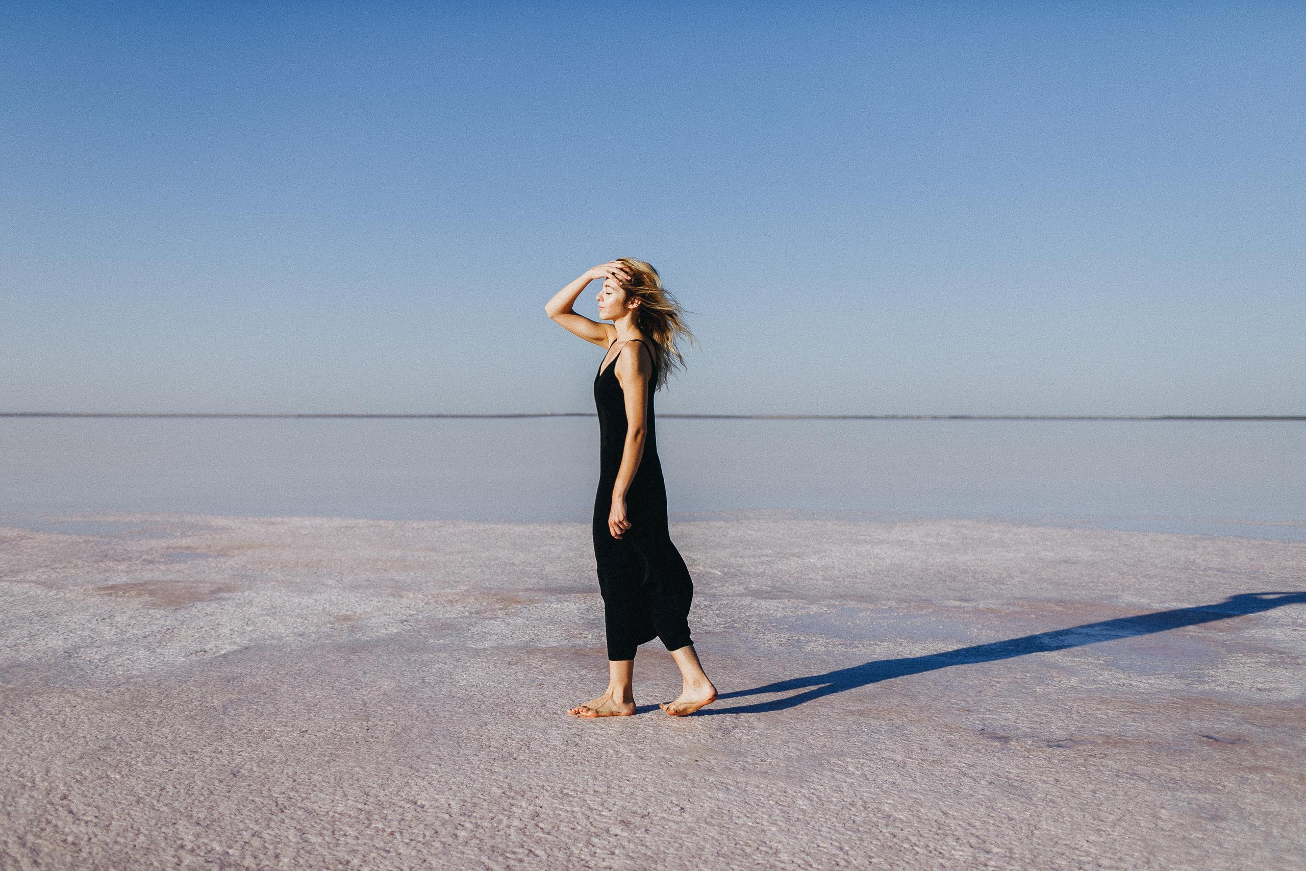 Девушка в черном платье гуляет по соленому розовому озеру. 