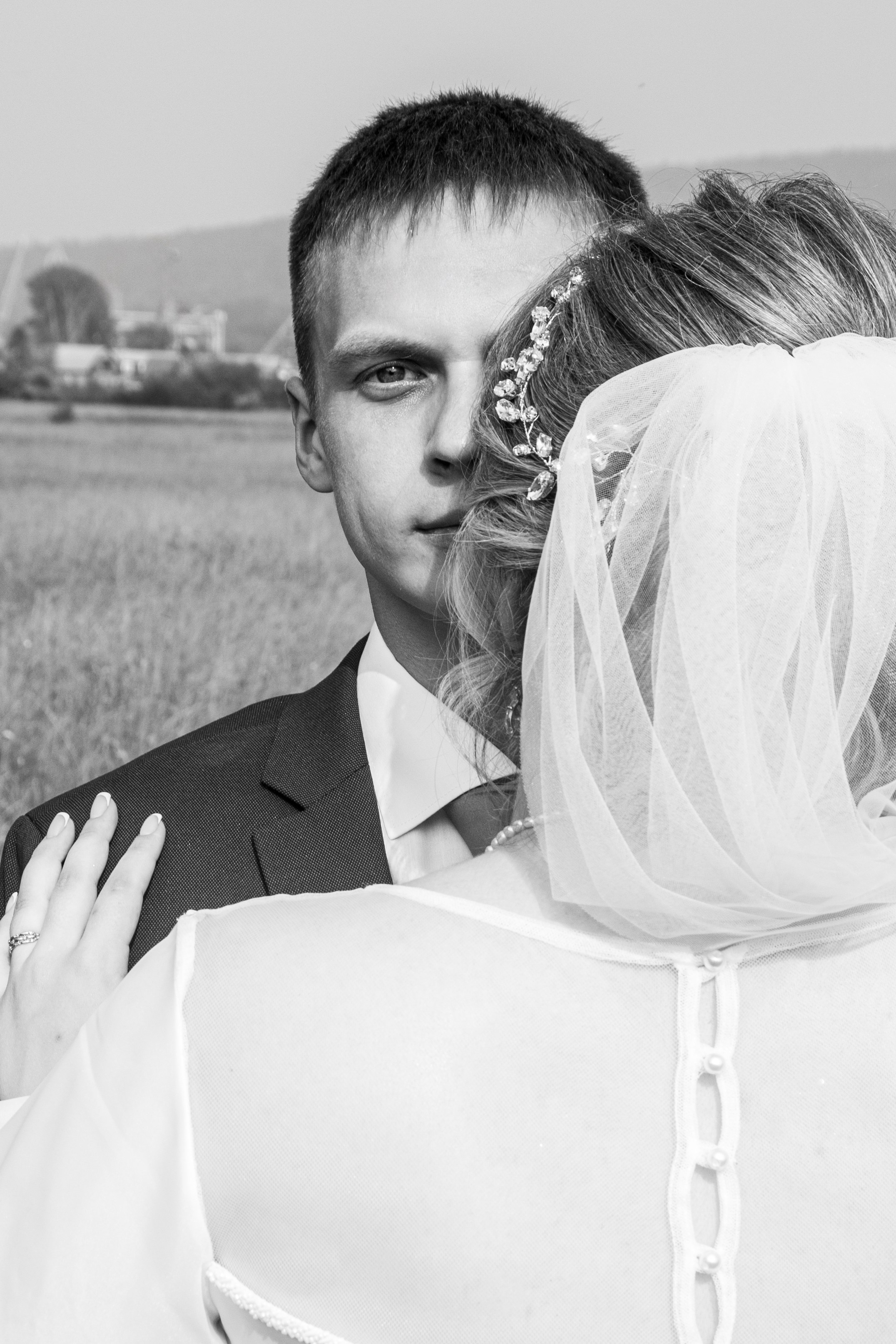 Чёрно-белое фото со спины — жених целует невесту, видна её причёска и платье.