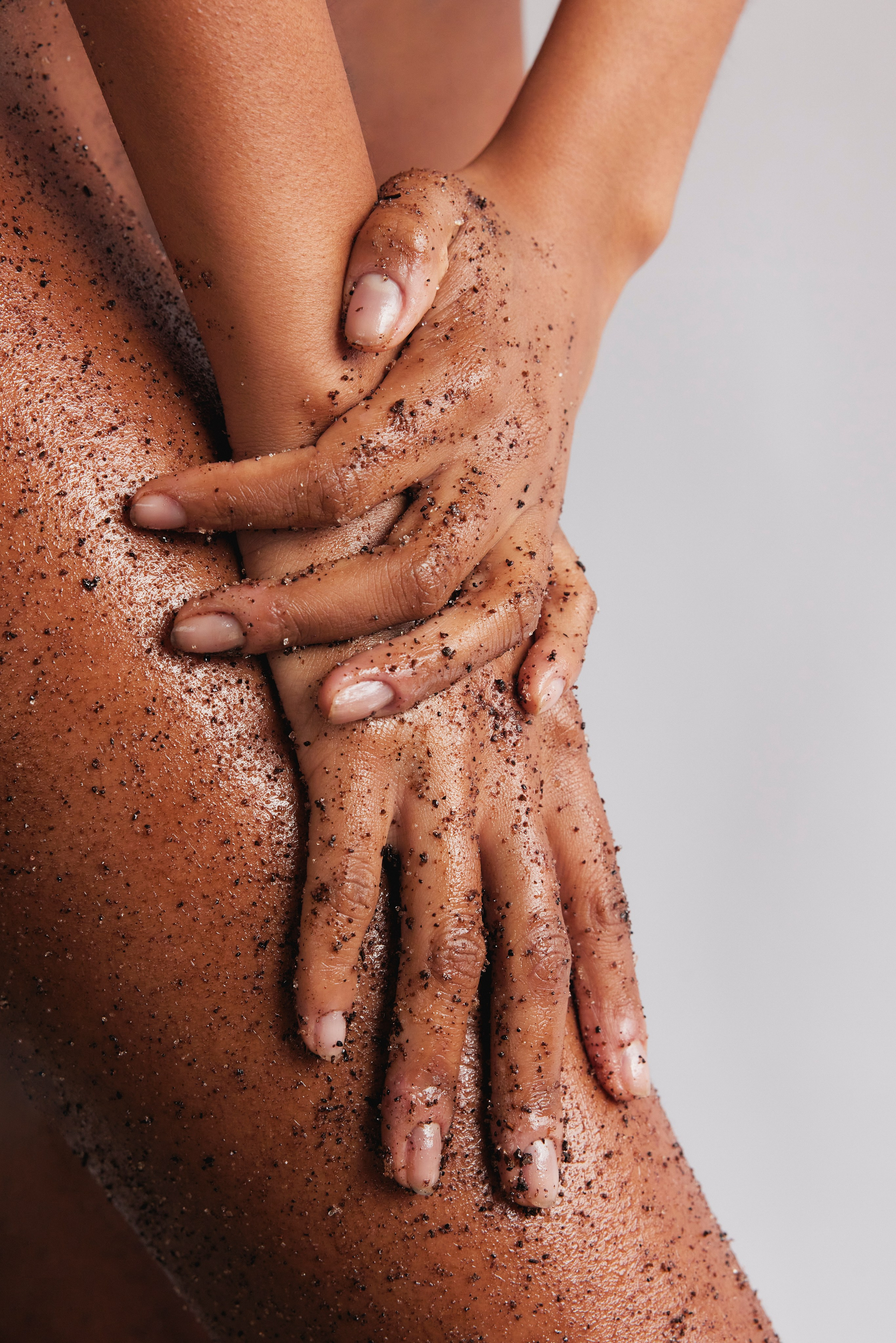 Hands gently massaging coffee scrub onto legs, highlighting a luxurious skincare experience.