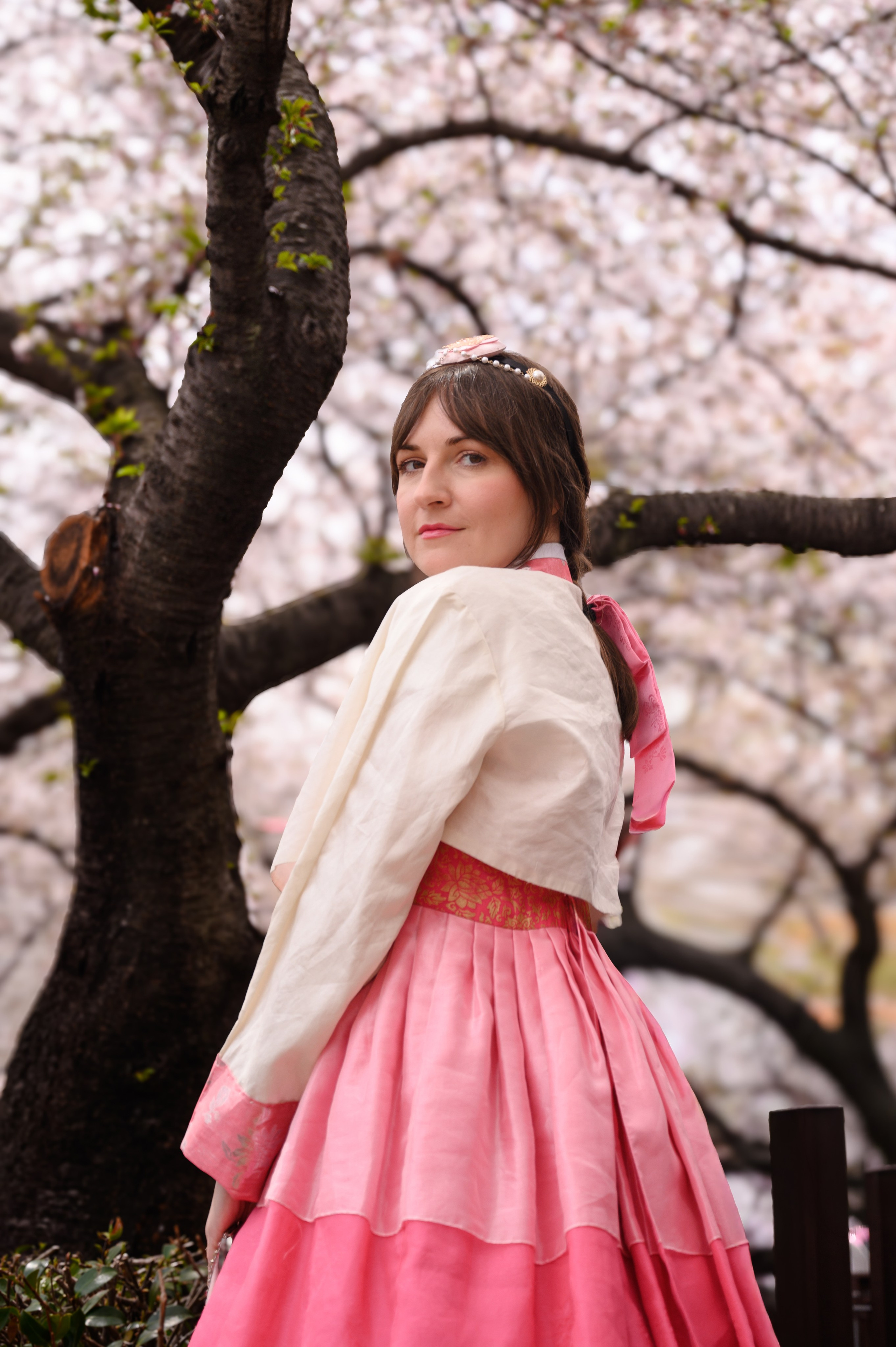 Woman in a pink hanbok under blooming cherry blossoms — hanbok photoshoot in Busan · 감천문화마을