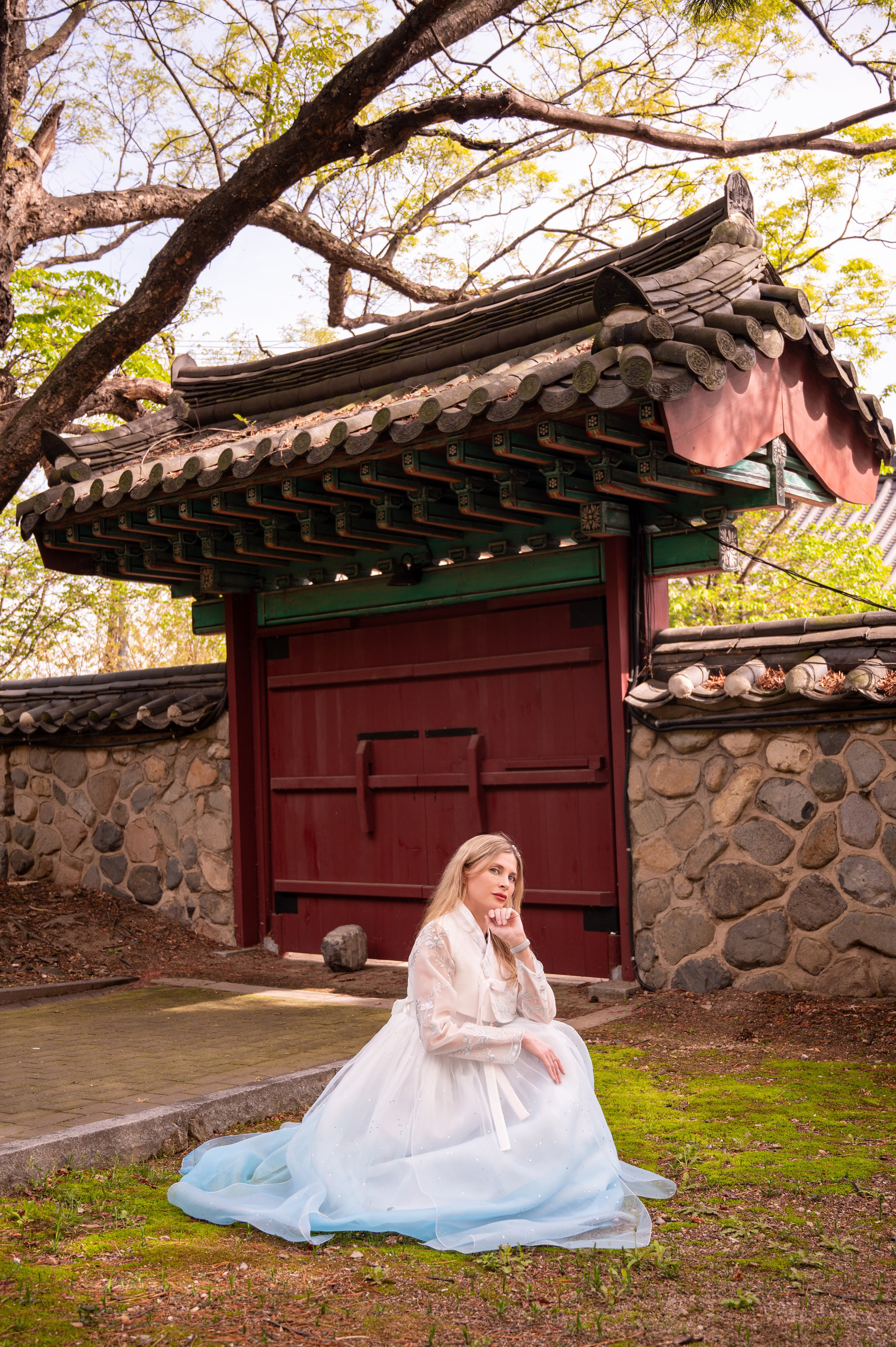 Woman in a pastel hanbok sitting by traditional gates — hanbok photoshoot in Busan · 釜山韩服写真