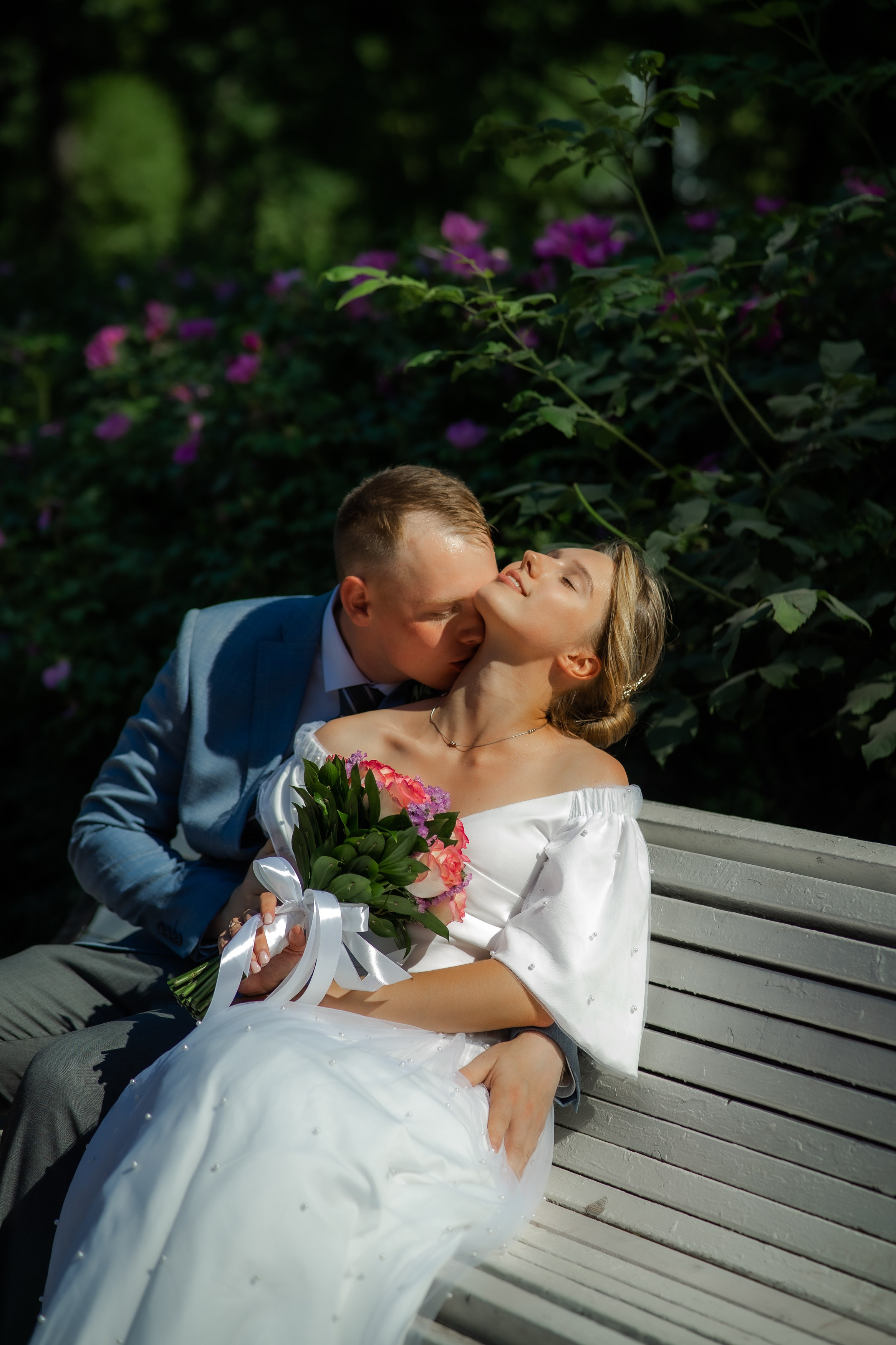 жених и невеста в свадебной фотосессии летом в Таврическом саду целуются на скамейке