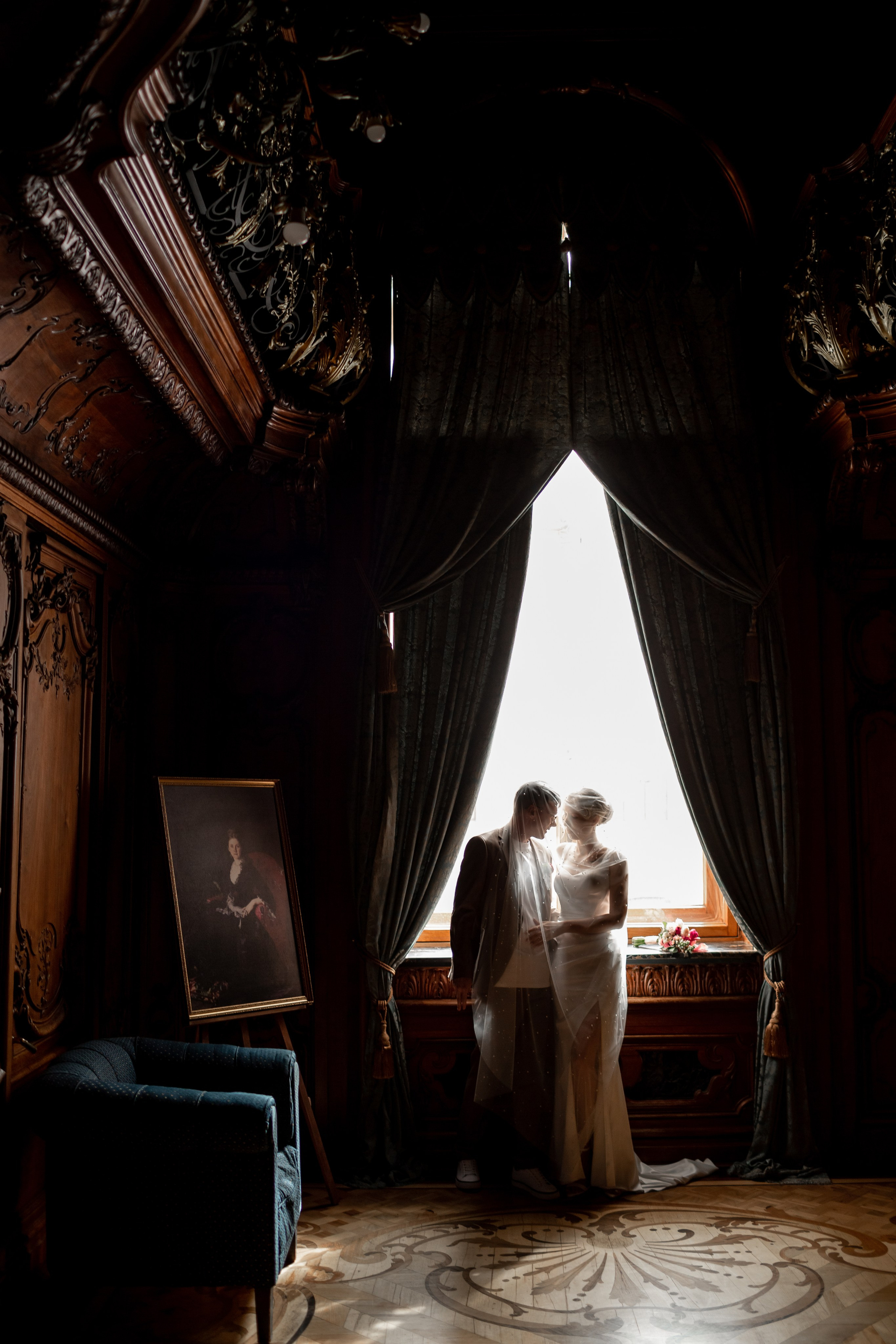 Красивая свадебная фотография: молодожены спрятались под фатой около окна в особняке.