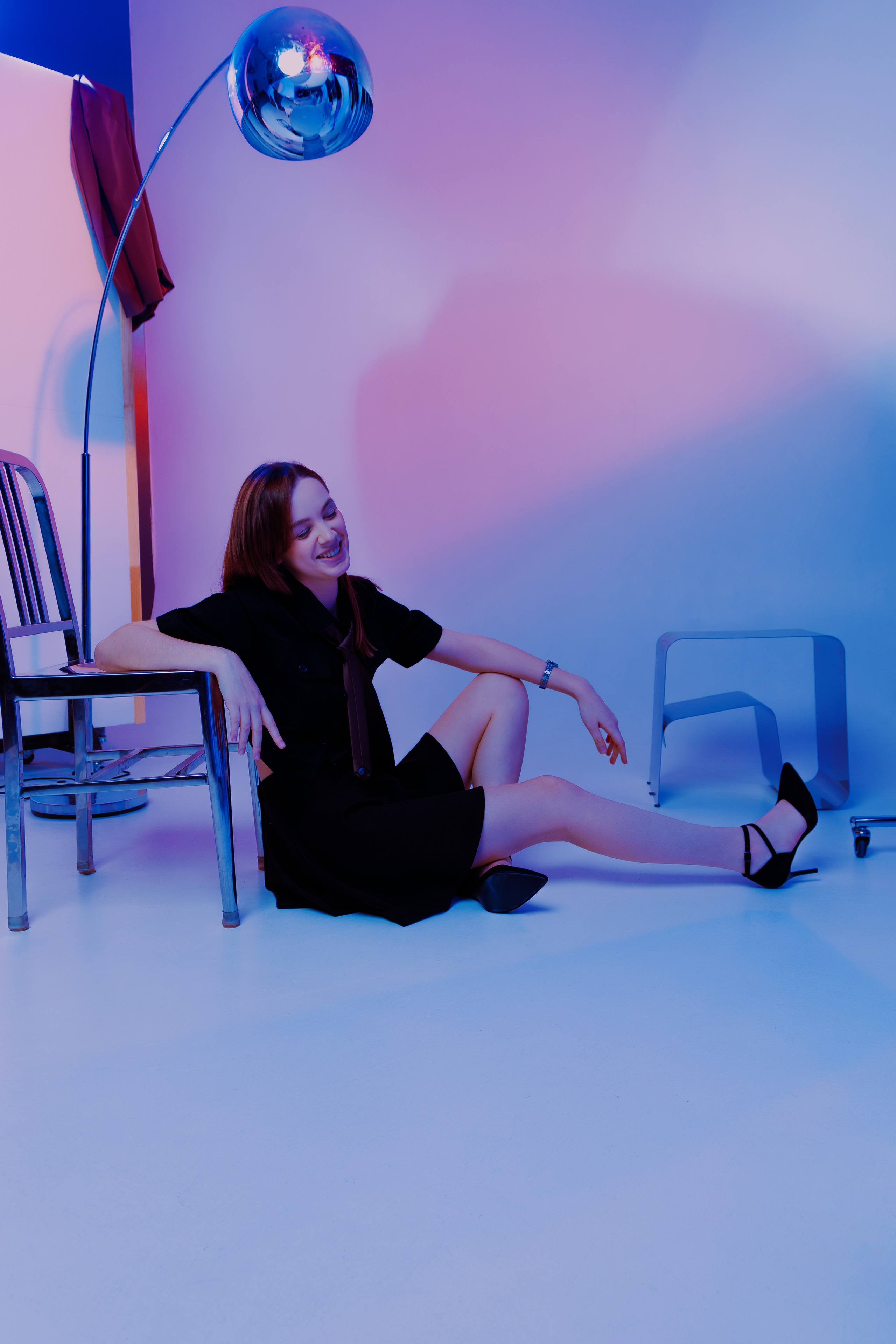 Студия в неоновых оттенках, модель на стуле — стильная фотосессия с игрой света и тени. Хромированная лампа добавляет футуристичности кадру.